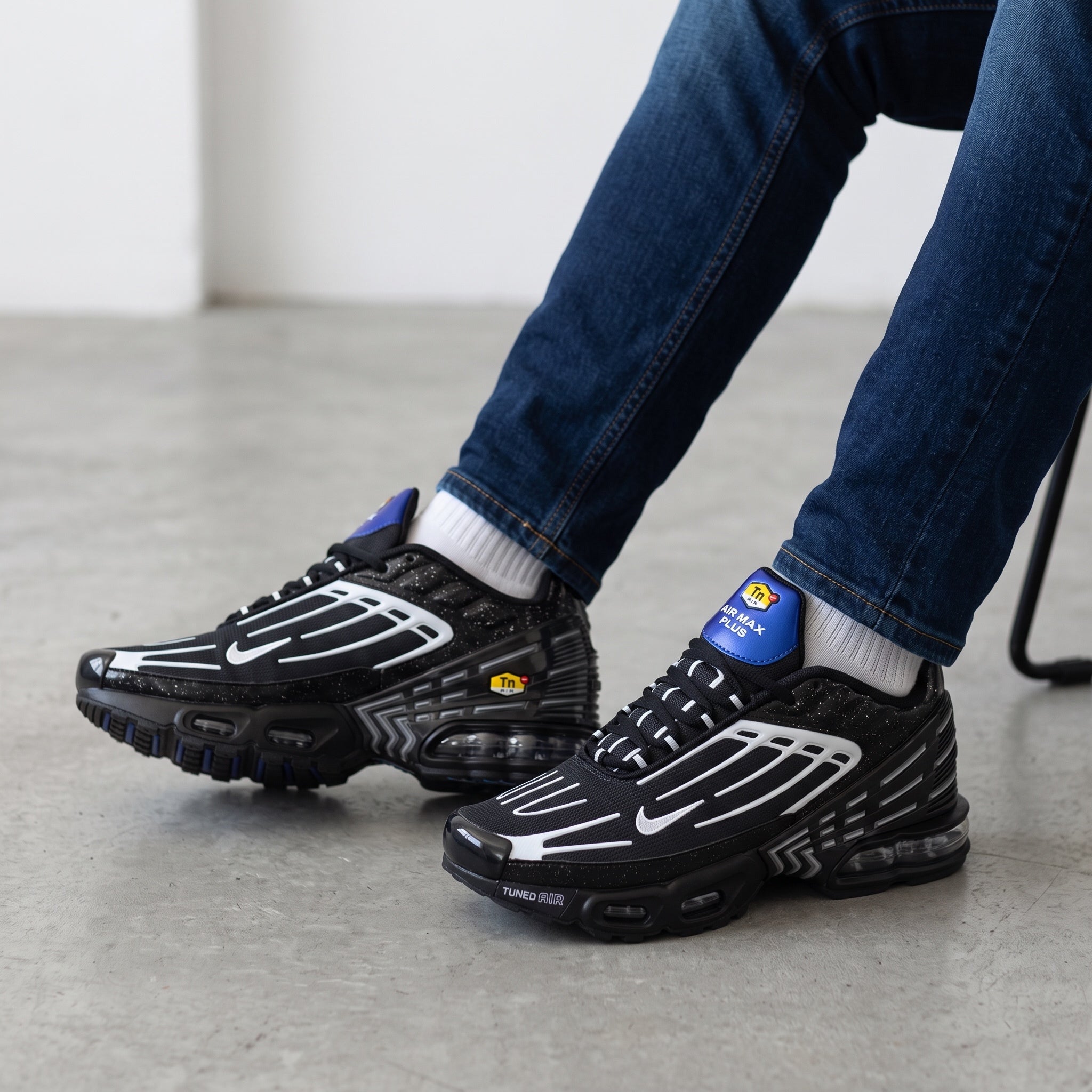Pair of black Nike Air Max Plus Tuned Air sneakers with white overlays and blue heel tab