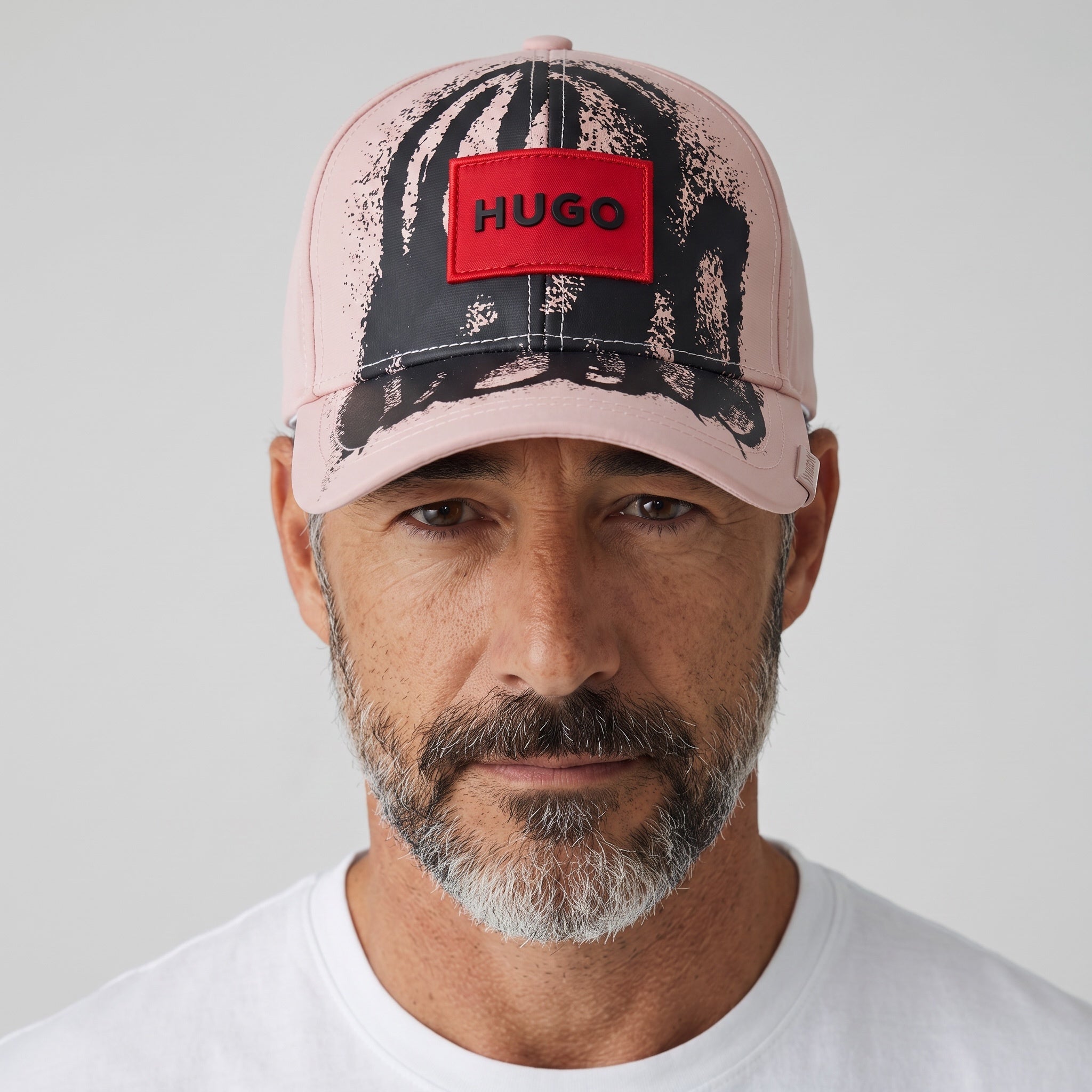 Man wearing a pink HUGO baseball cap with black splatter print and red logo patch