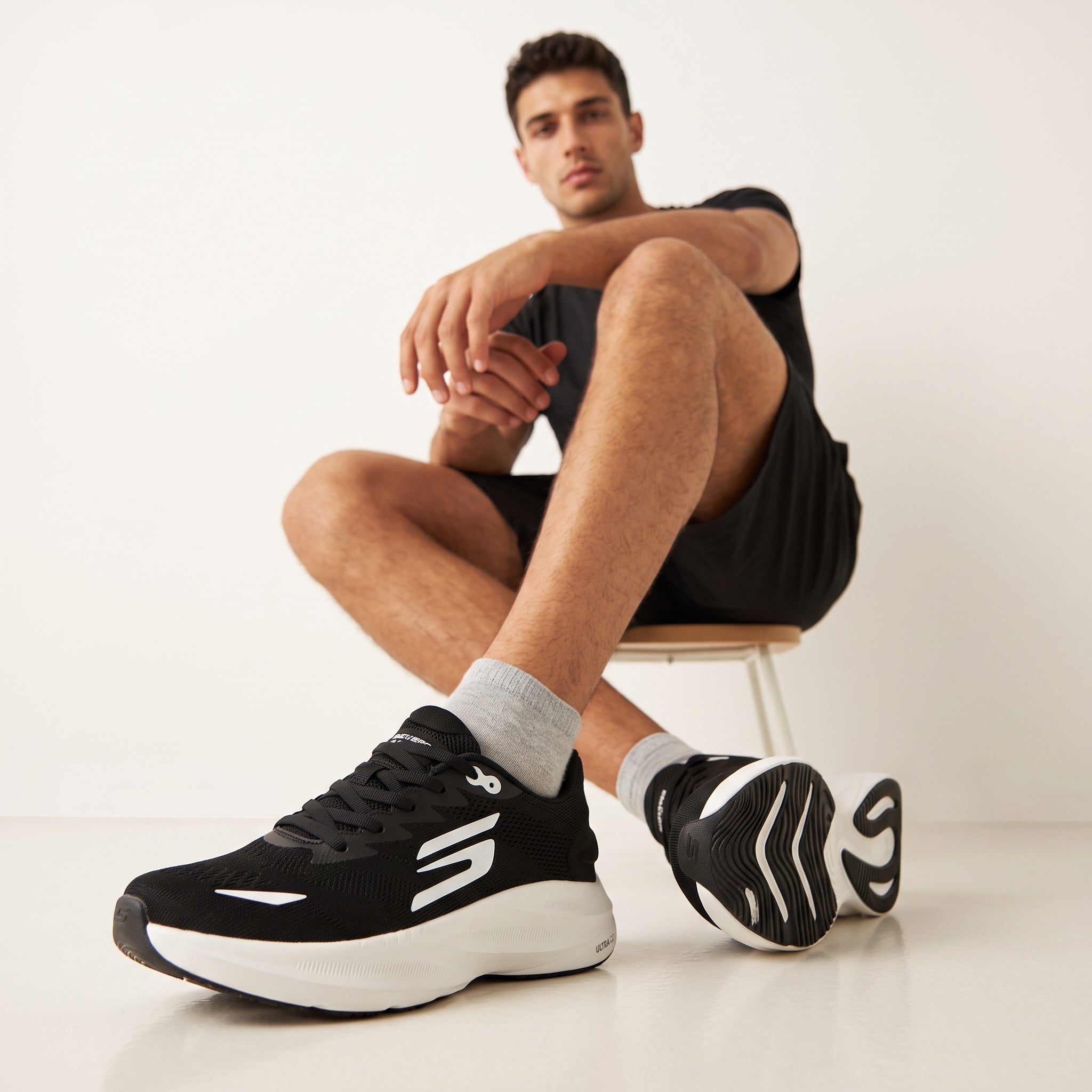 Black and white Skechers mesh sneakers with sculpted white sole on seated model