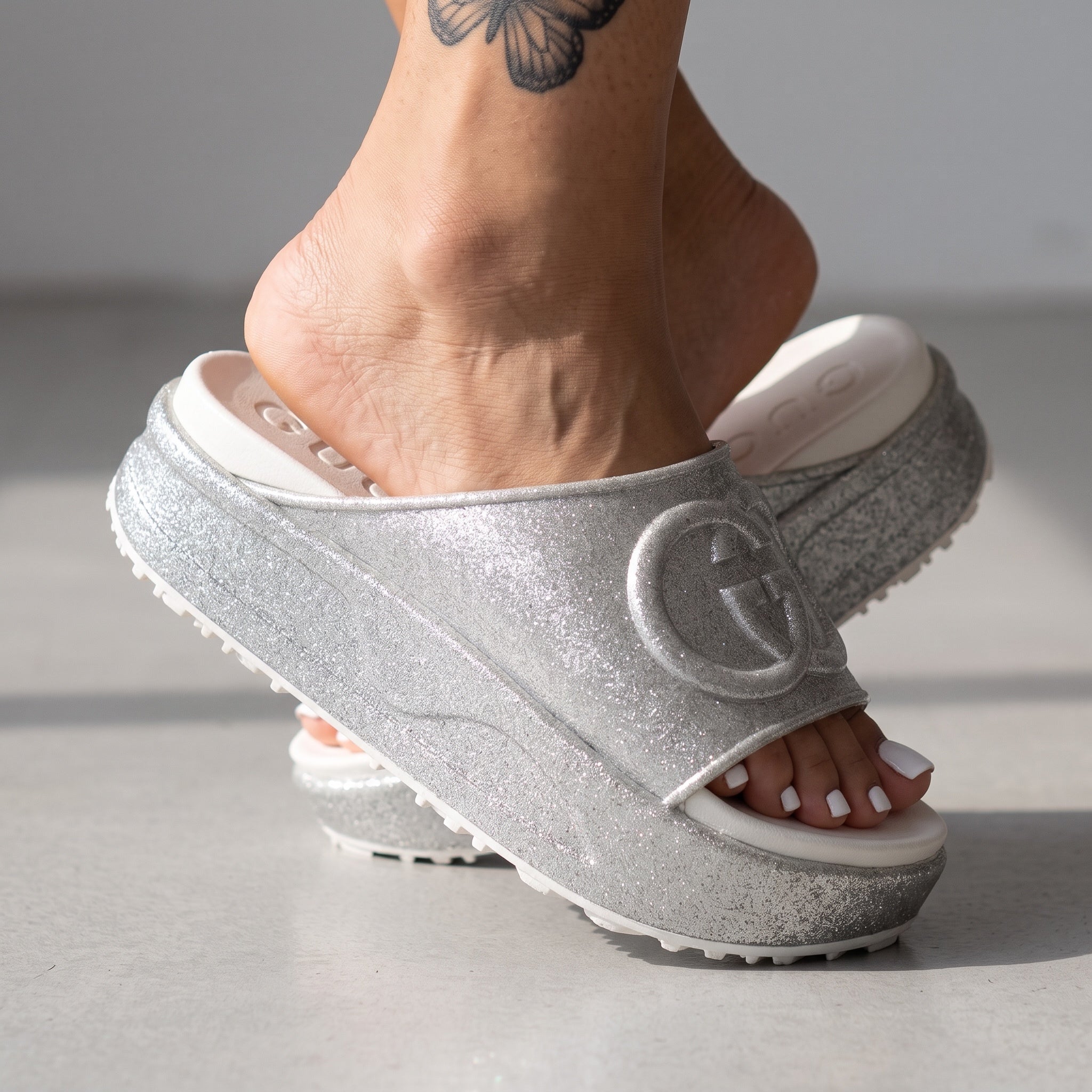 Silver Gucci flatform slides with glitter finish and raised interlocking G logo on white footbed
