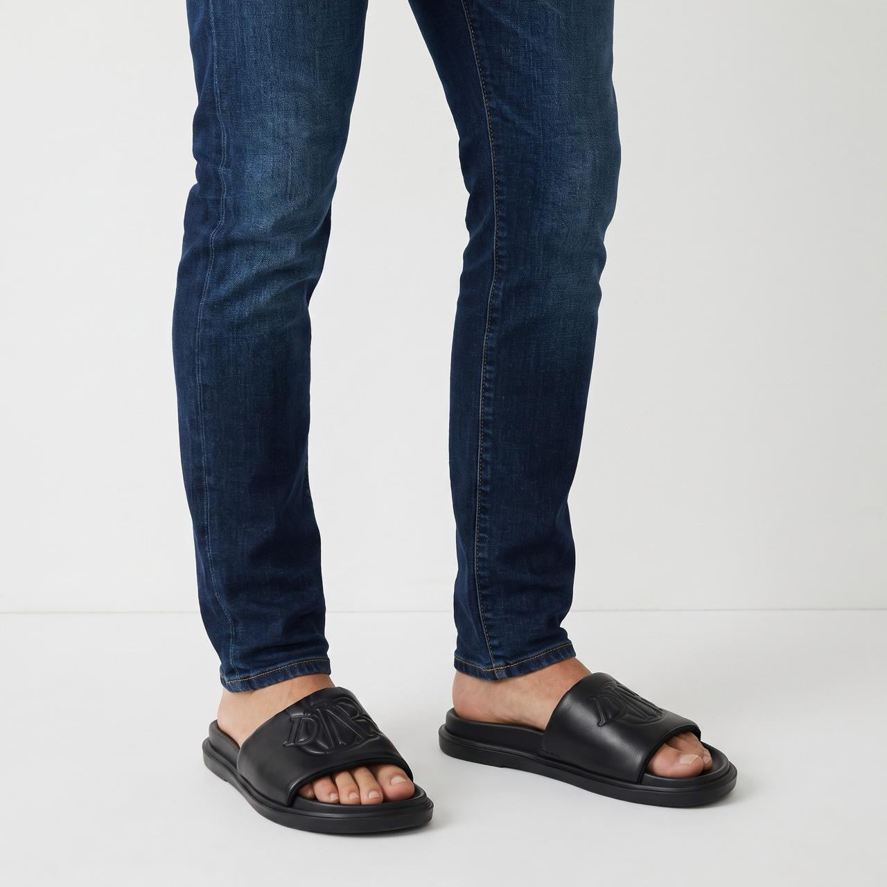 Black Dior men's slides with embossed logo on strap, worn with jeans
