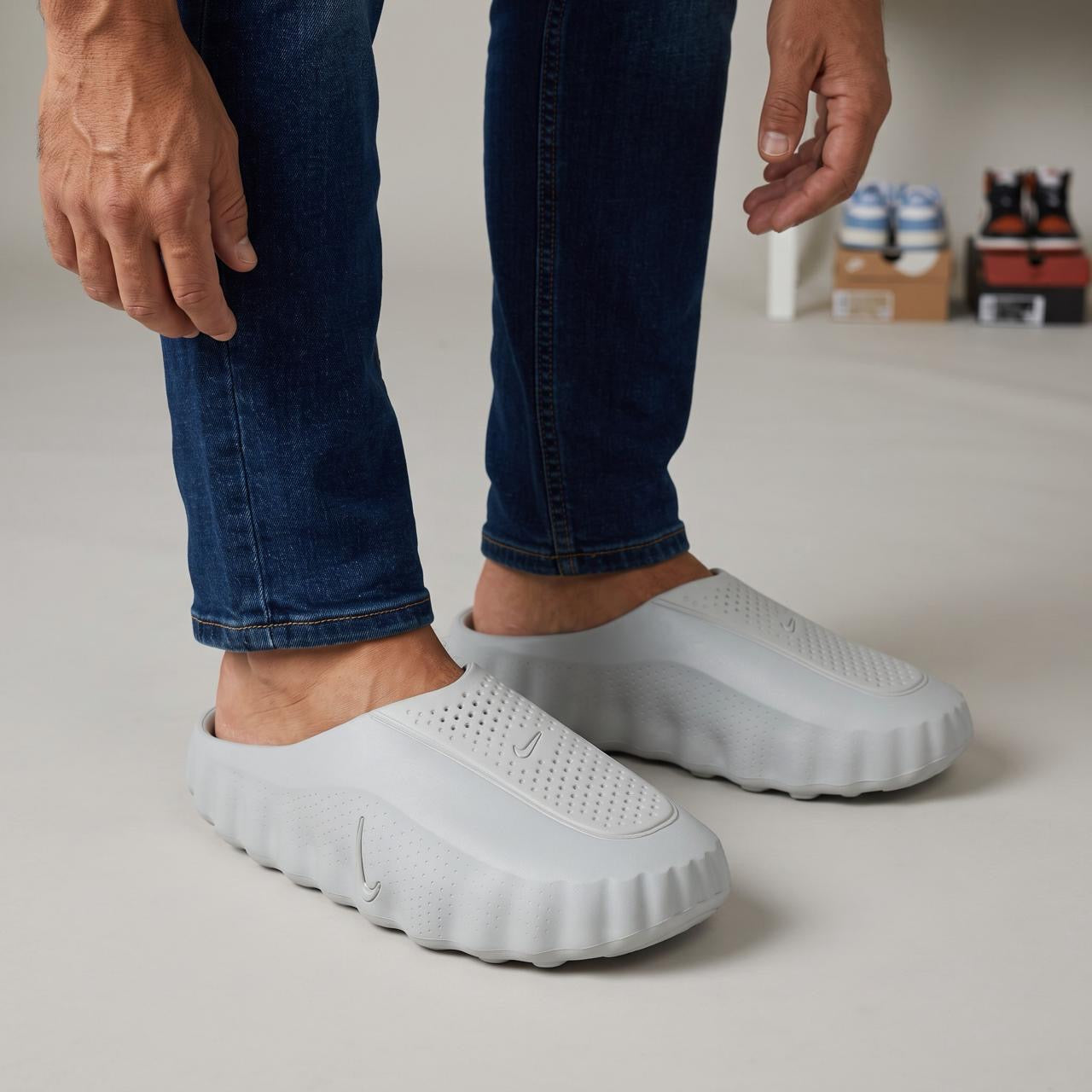 Pair of light grey Nike foam slip-on mules shown on feet