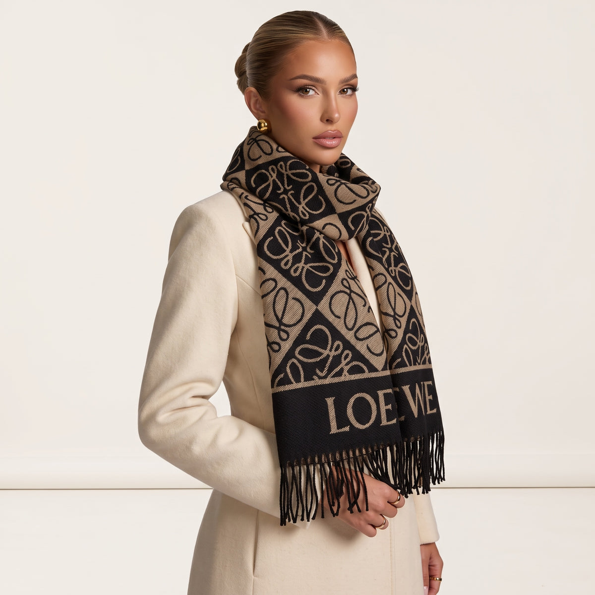 Black and tan Loewe logo jacquard scarf with fringe draped over cream coat