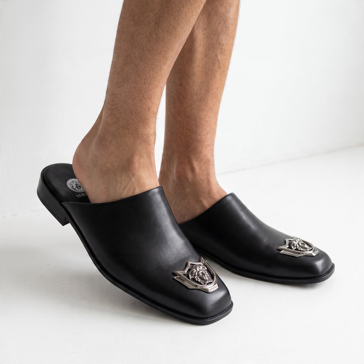 Black Versace mules with metal Medusa badge shown on model feet