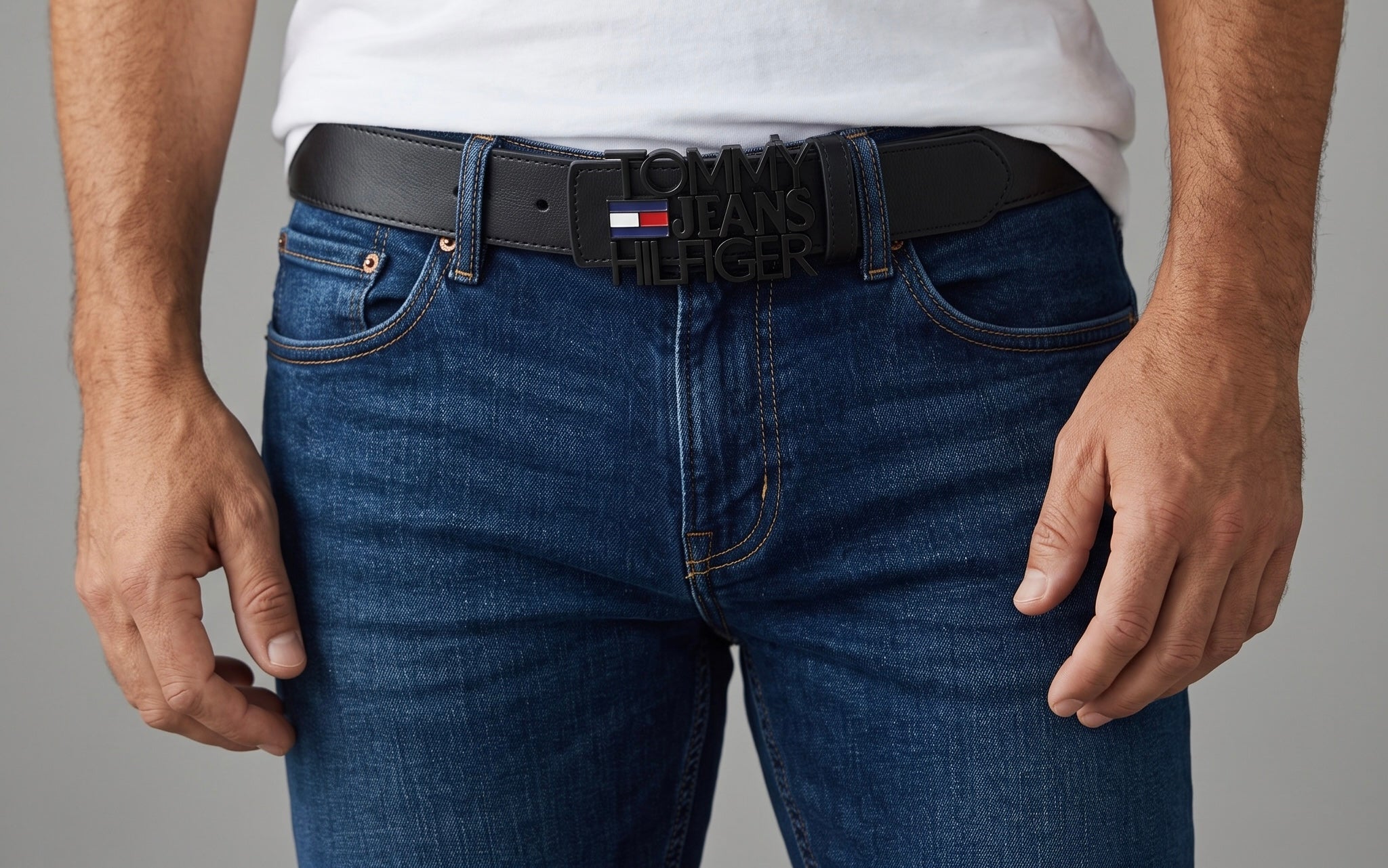 Black Tommy Jeans belt with large black logo buckle and small red white blue flag detail worn with jeans