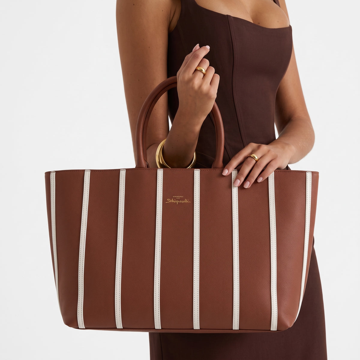 Brown Schiaparelli tote bag with white vertical stripes and gold keyhole plaque, shown with rolled top handles