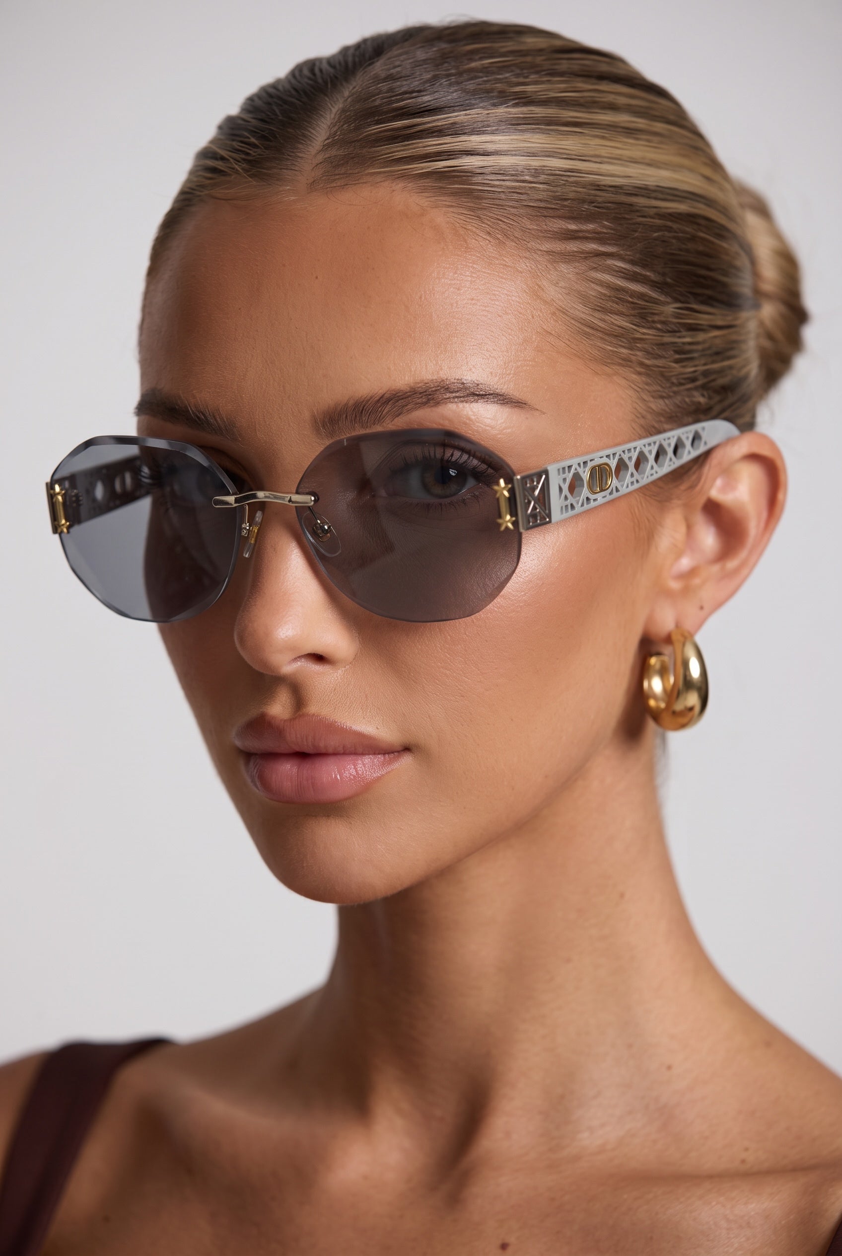 Rimless grey sunglasses with lattice patterned light grey temples and gold accents