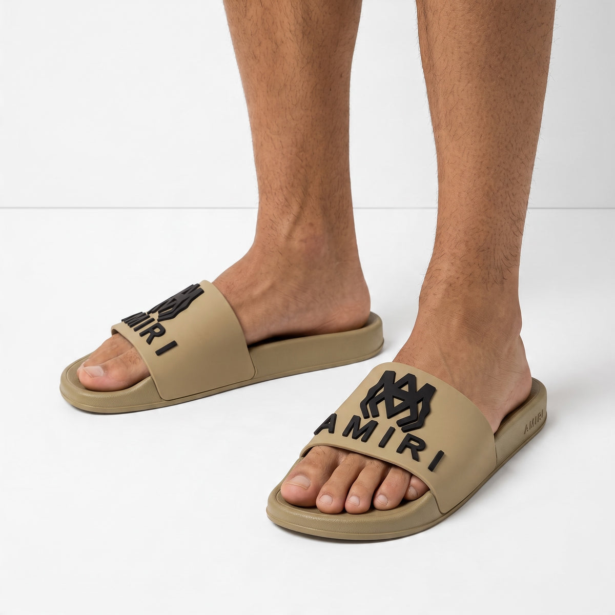 AMIRI beige rubber slides with black logo on model feet
