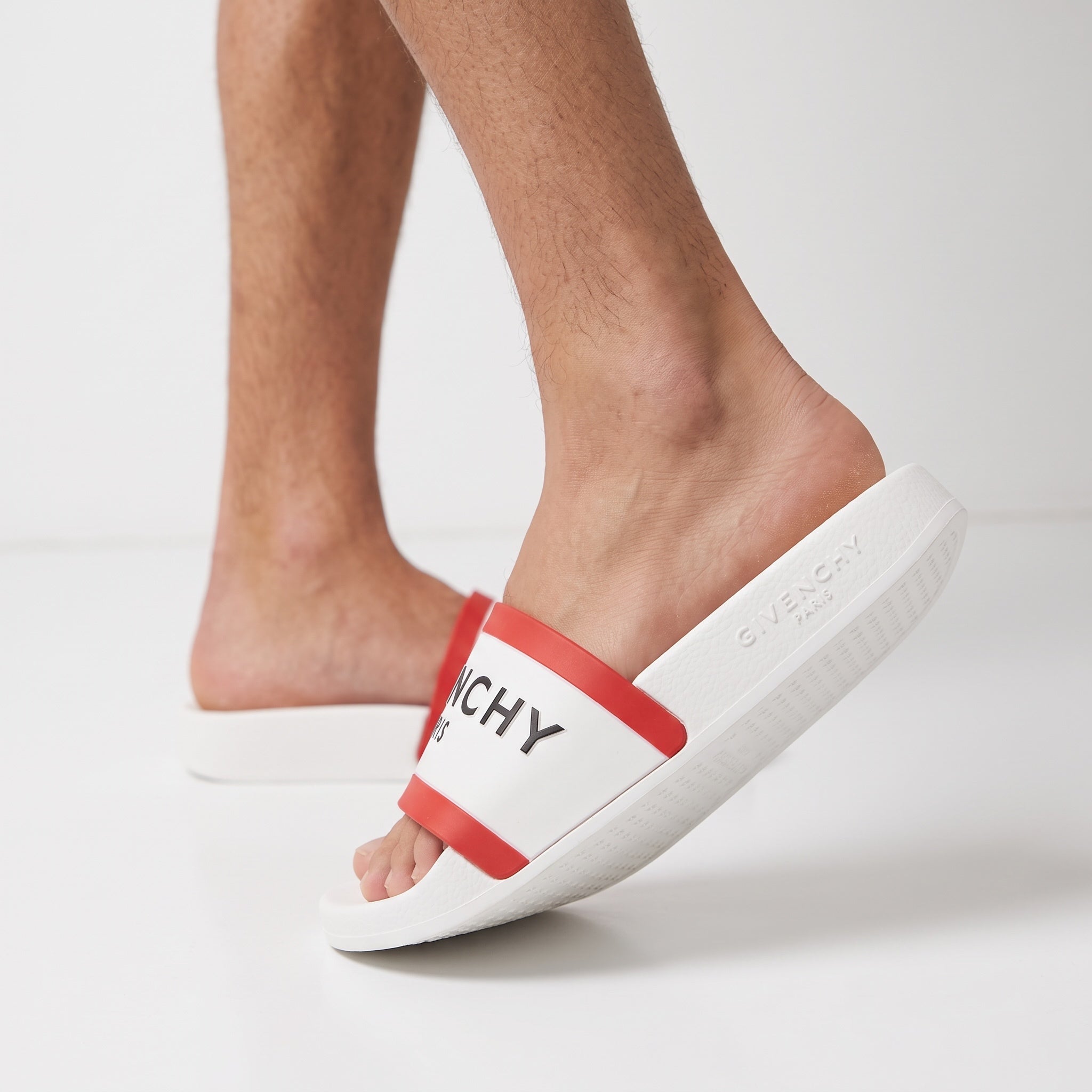 White Givenchy slide with red trim and black logo on a man's foot