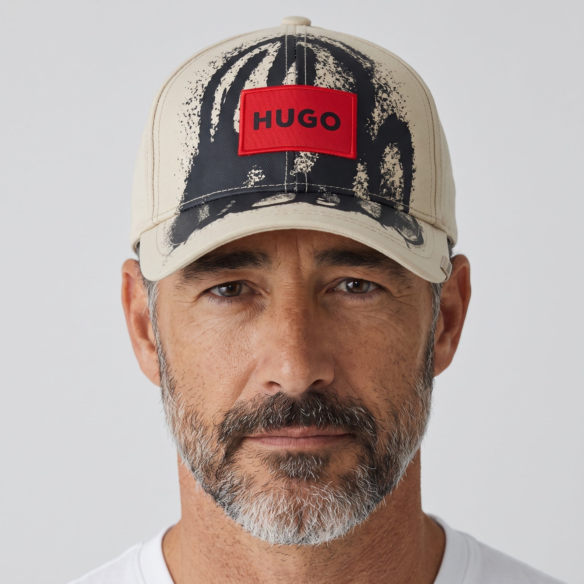 Man wearing a beige and black splatter print HUGO baseball cap with red logo patch