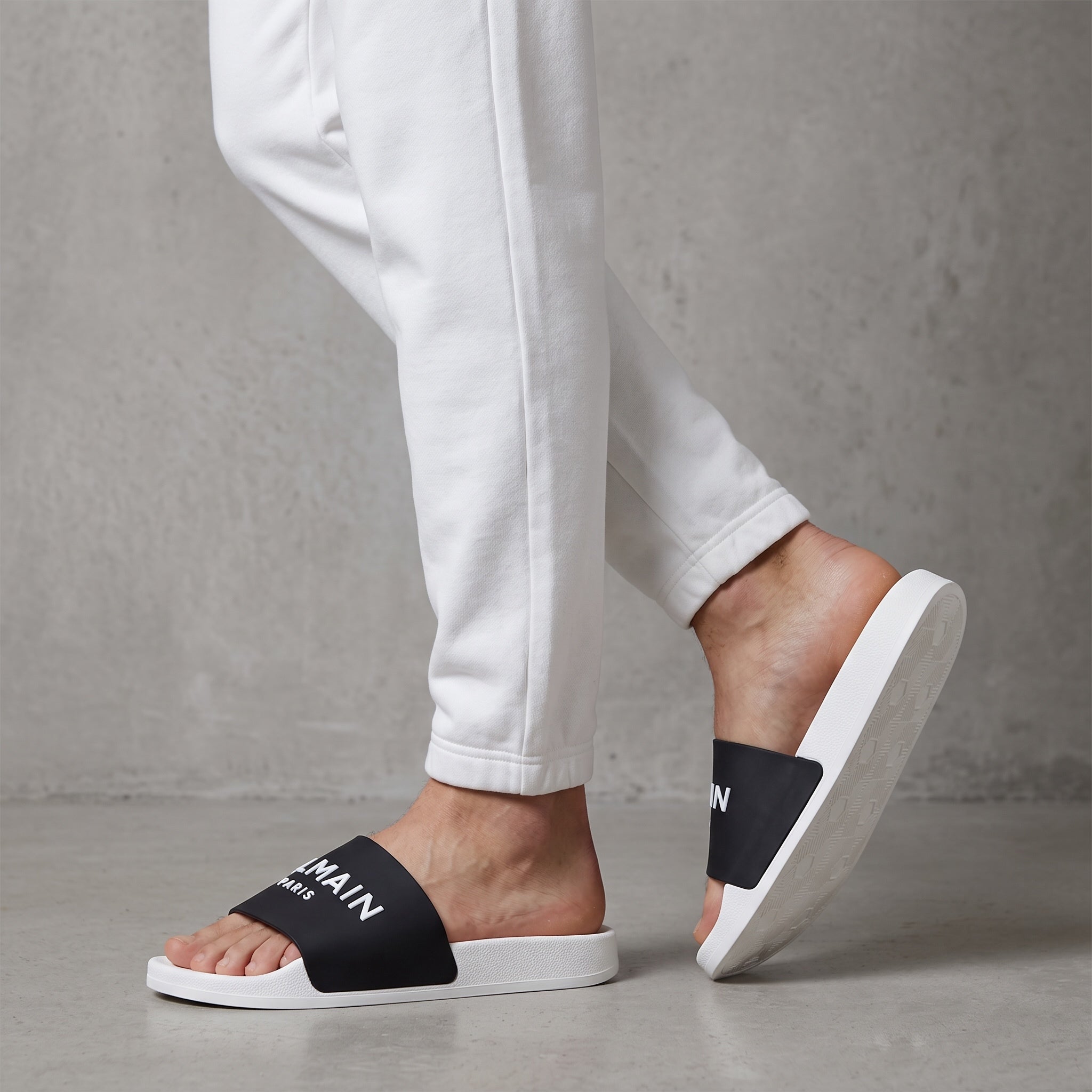 Black Balmain logo slide sandals with white sole seen on model feet