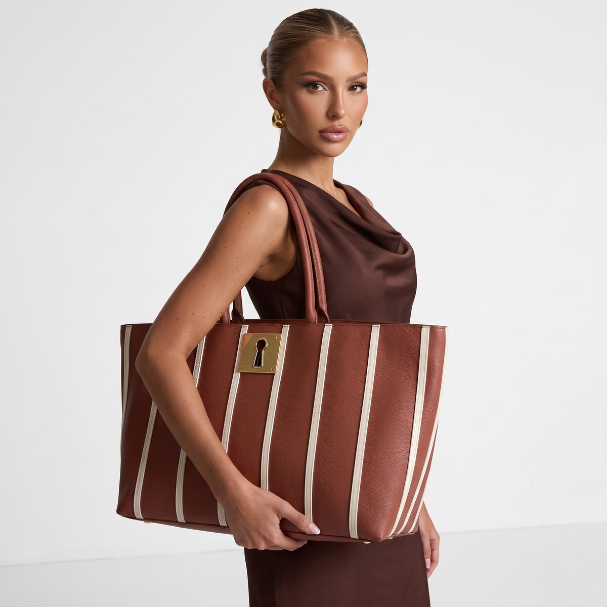 Brown Schiaparelli tote bag with white vertical stripes and gold keyhole plaque, shown with rolled top handles