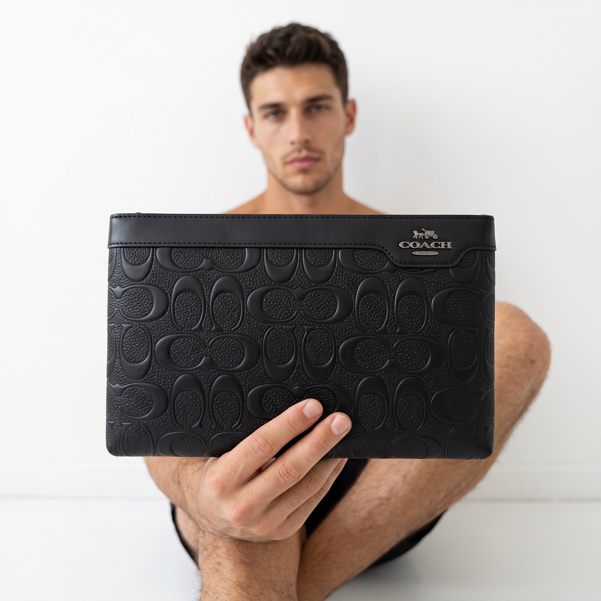 Black Coach embossed signature clutch with metal logo held by a model