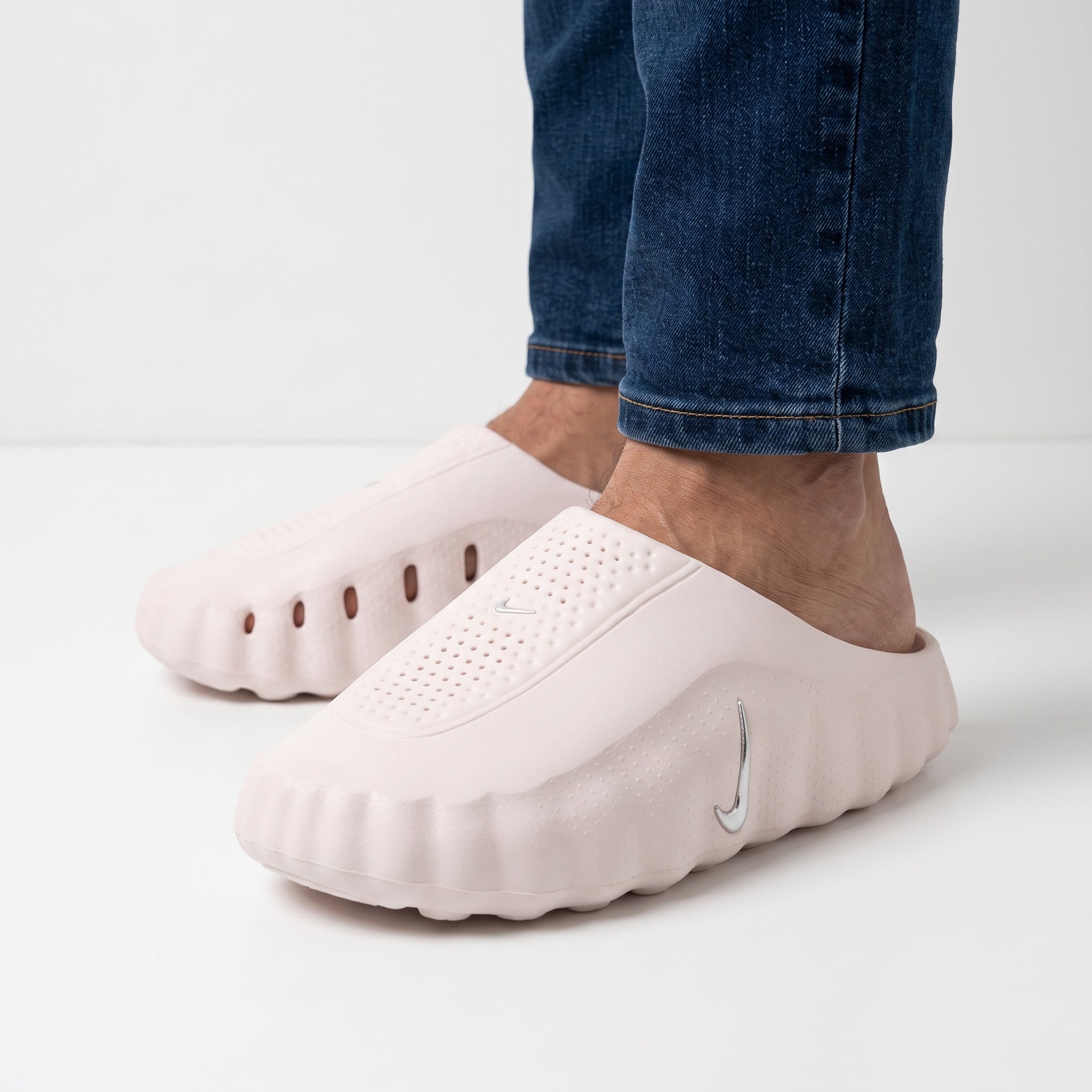 Pale pink Nike slip-on clogs with perforated upper and silver swoosh