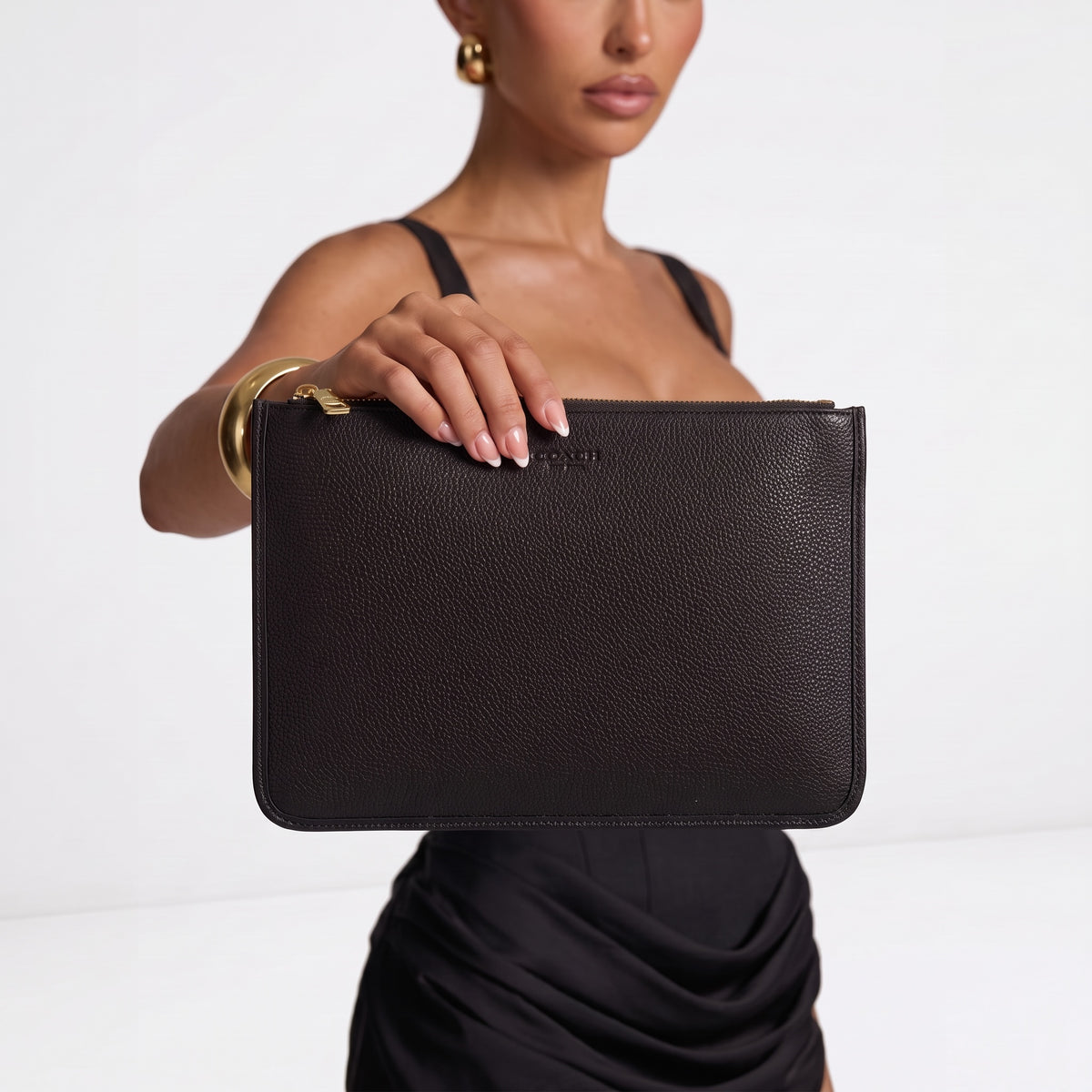 Black pebbled Coach zip pouch with gold zipper held by model