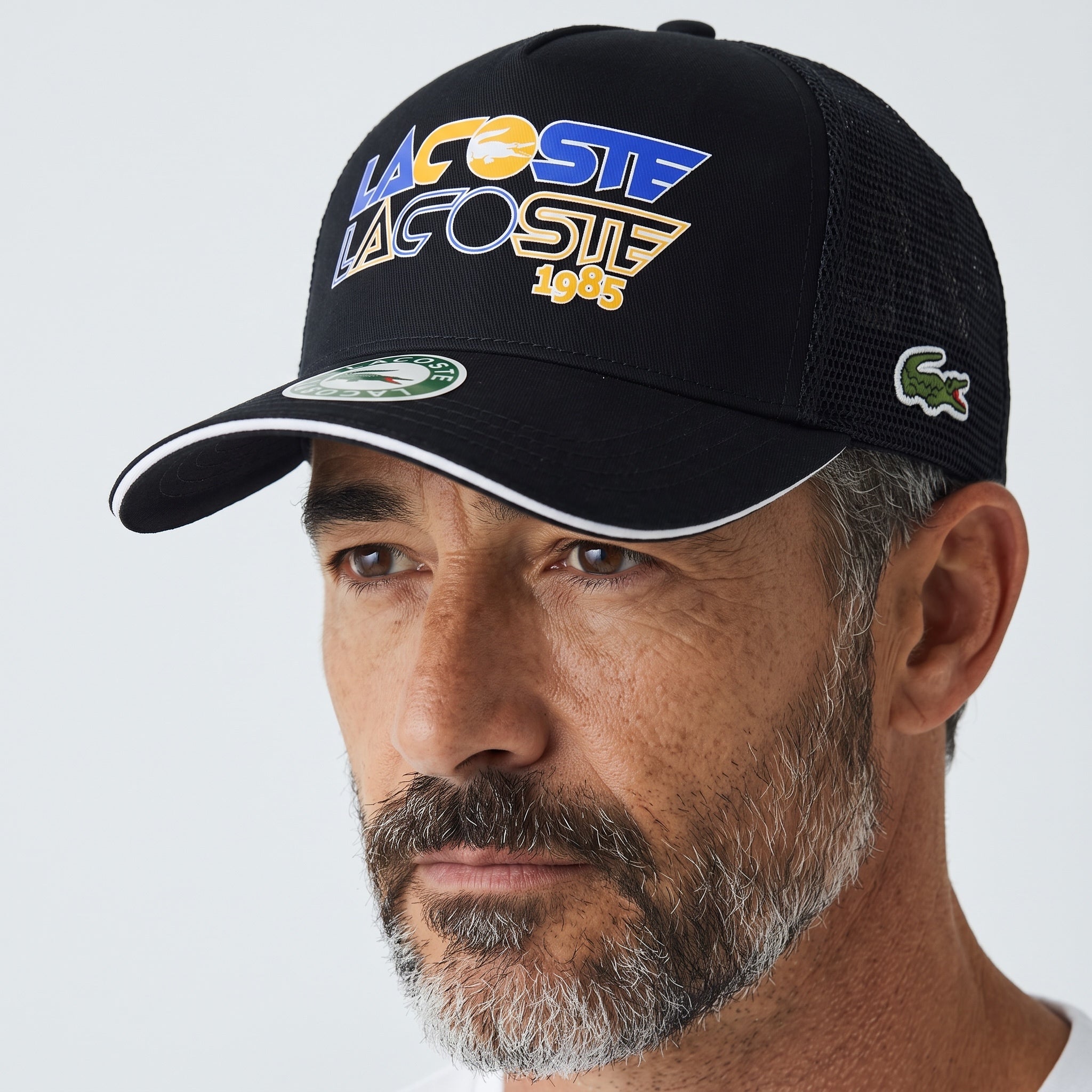 Man wearing a black Lacoste 1985 mesh trucker cap with crocodile logo