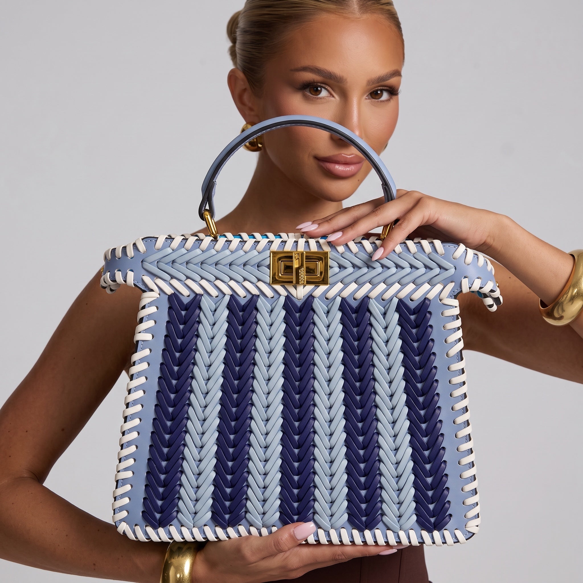 Light blue woven top-handle bag with white whipstitch trim and gold turn-lock clasp
