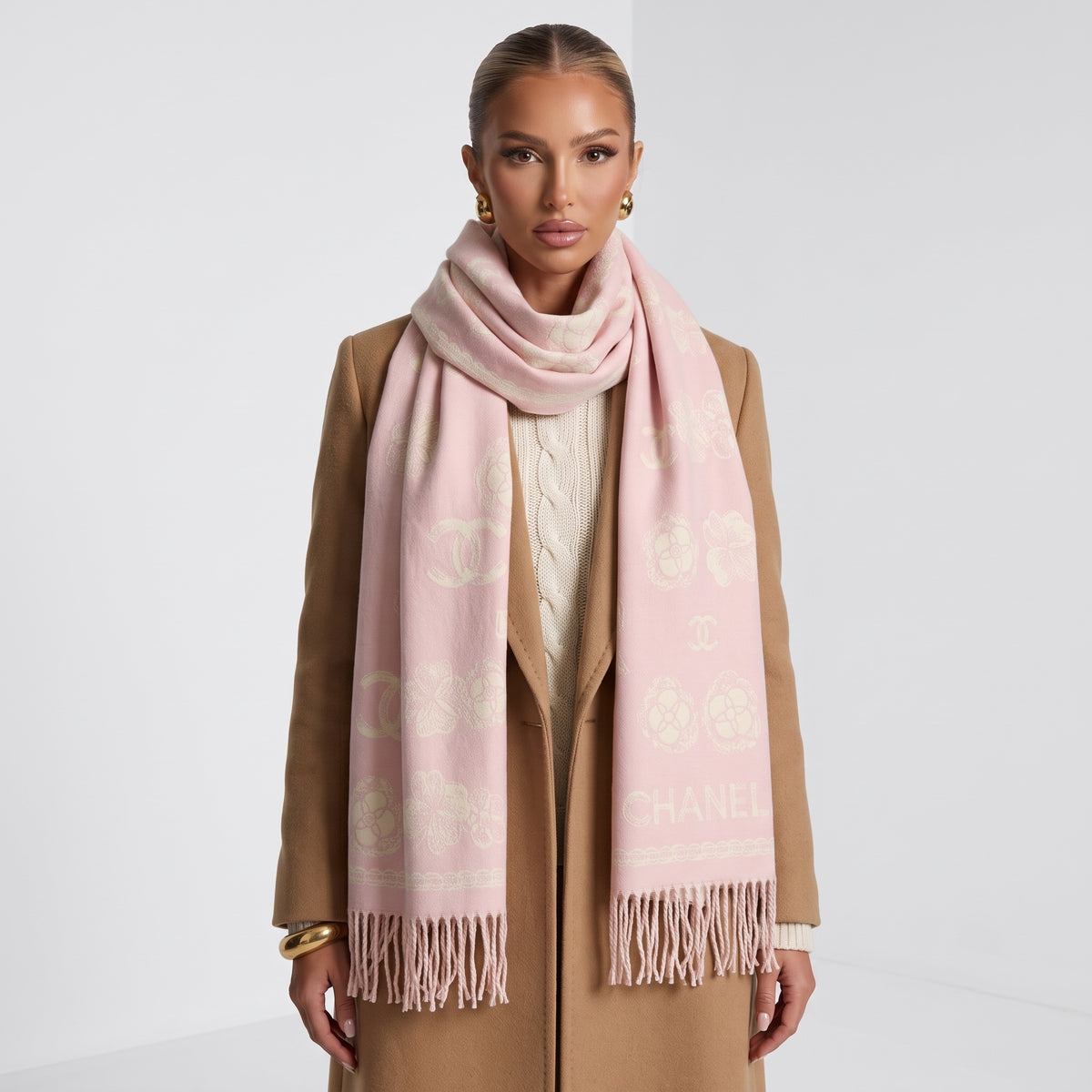 Pale pink Chanel scarf with repeated logo and camellia motifs and long fringe, draped over coat