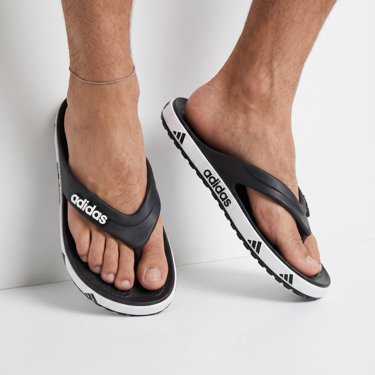 black adidas flip-flops with white adidas logo on strap and repeated logo on white midsole