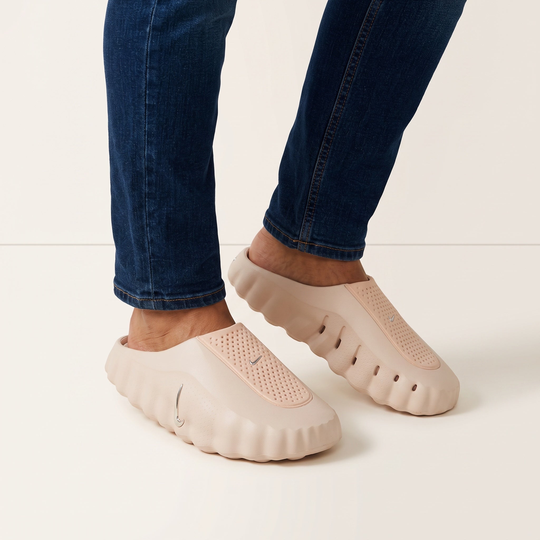 Blush pink one-piece Nike foam clogs with silver swoosh, slip-on style