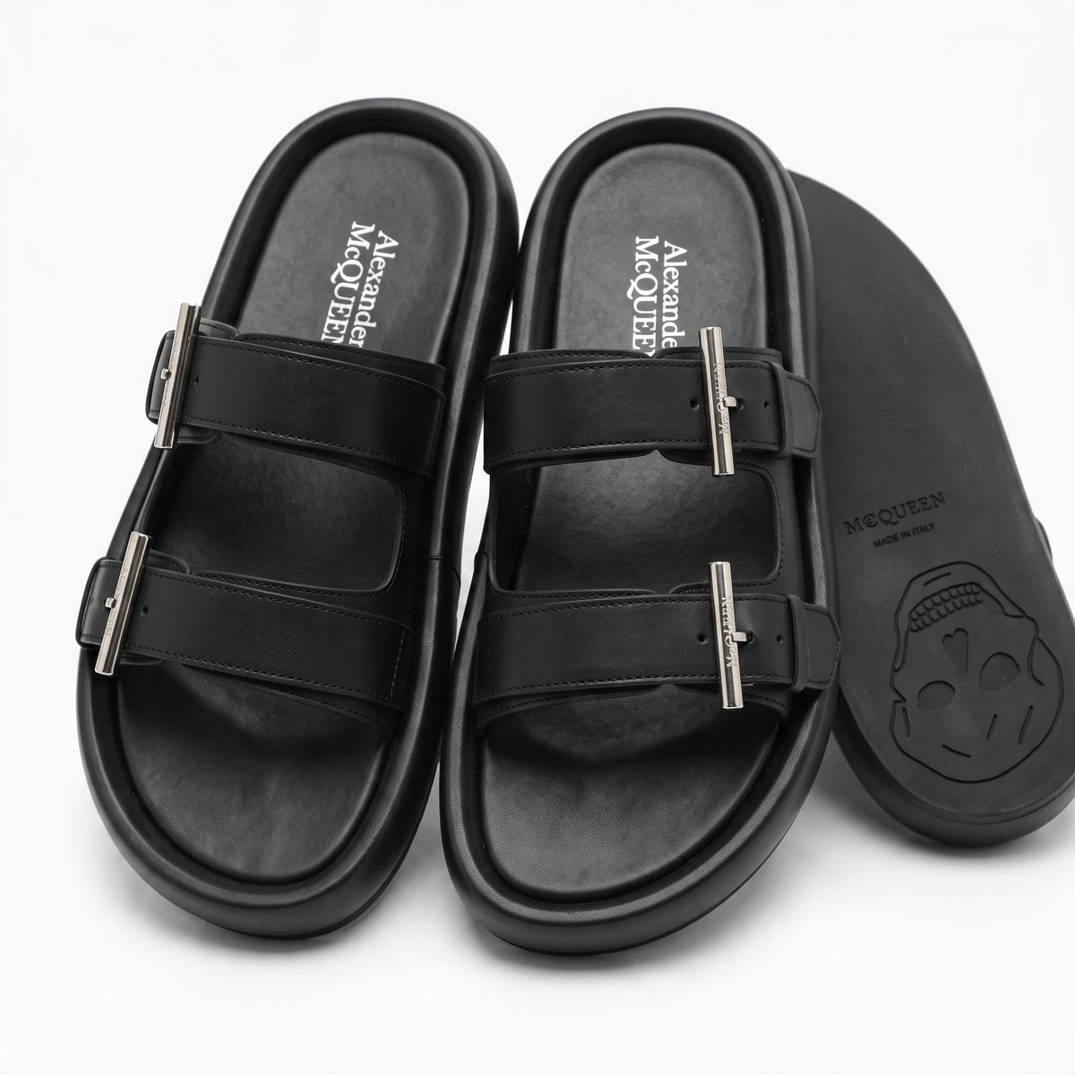 Pair of black Alexander McQueen double-strap slide sandals with metal buckles and skull embossed sole
