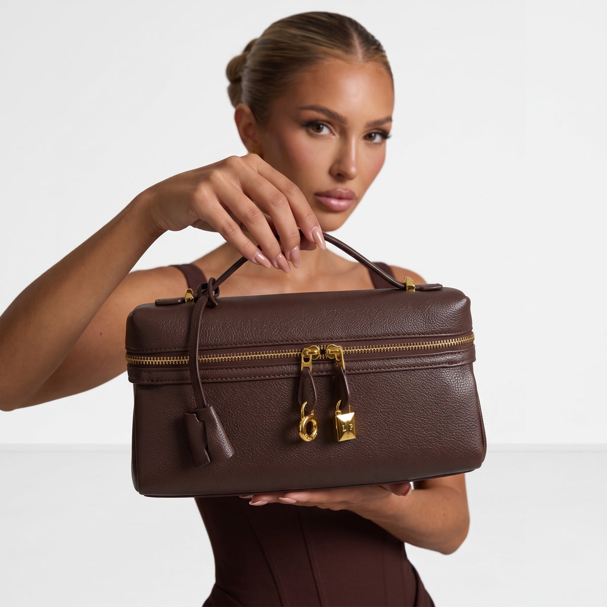 brown pebbled vanity bag with gold zips and padlock charms held by model