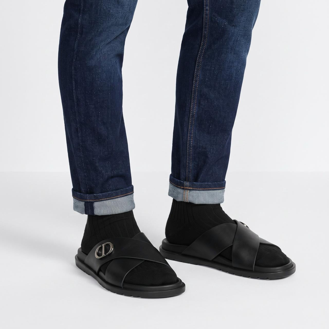 Black Dior crisscross slide sandal with metal CD logo and textured rubber sole, shown on model feet