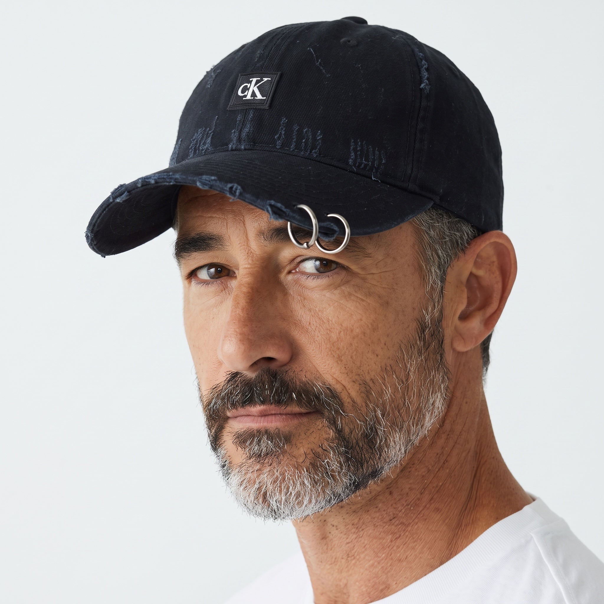 Man wearing a black distressed Calvin Klein baseball cap with cK logo patch