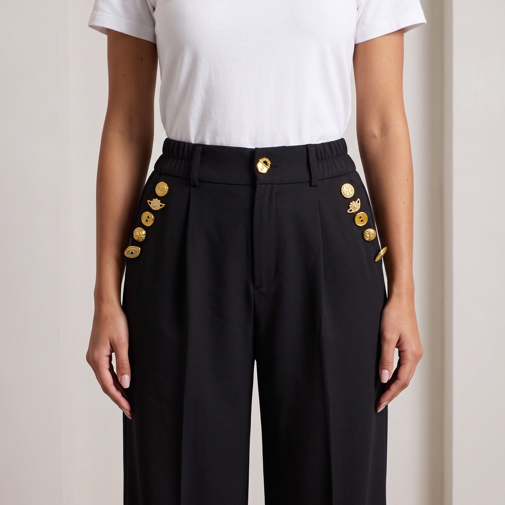 High-waist black trousers with gold decorative buttons down the sides and waist
