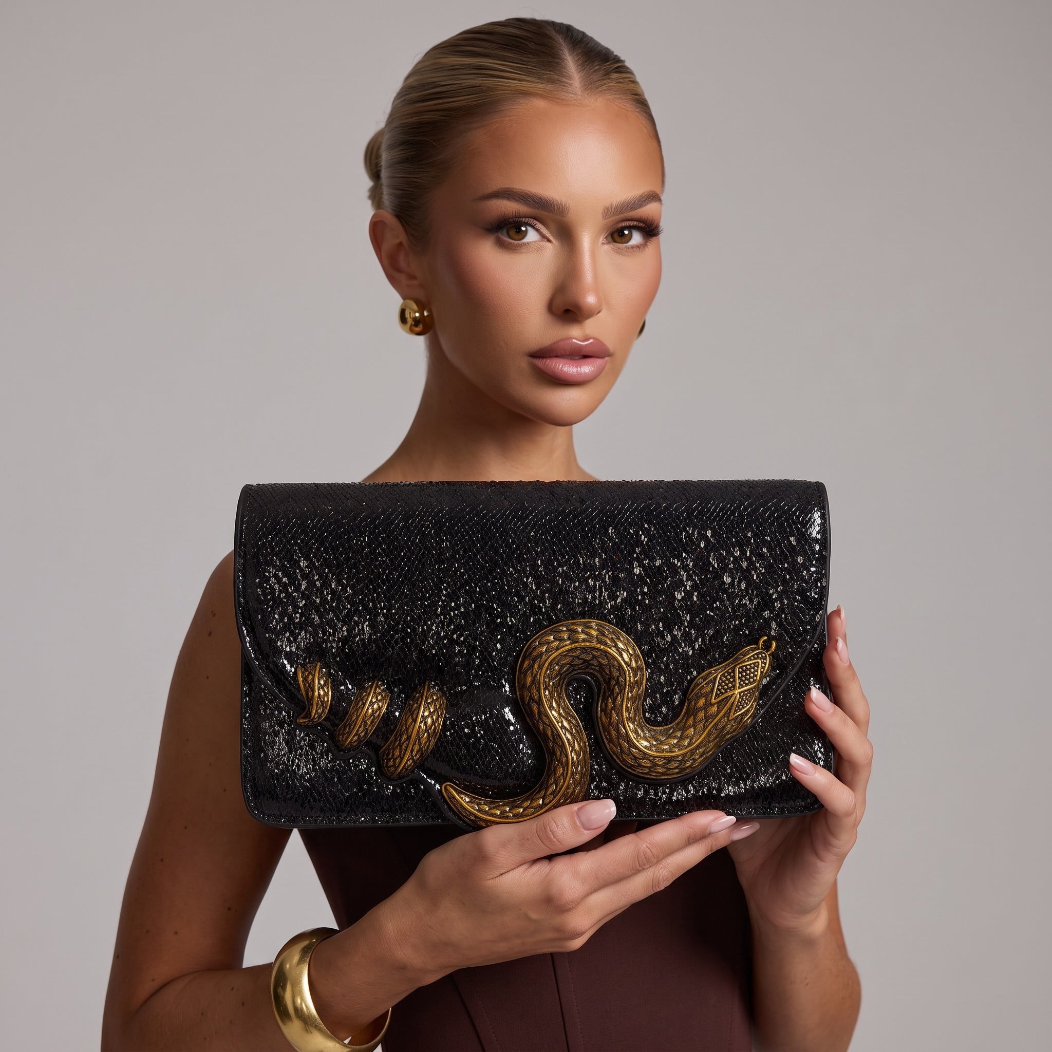 Black glossy clutch with large gold snake applique held by model