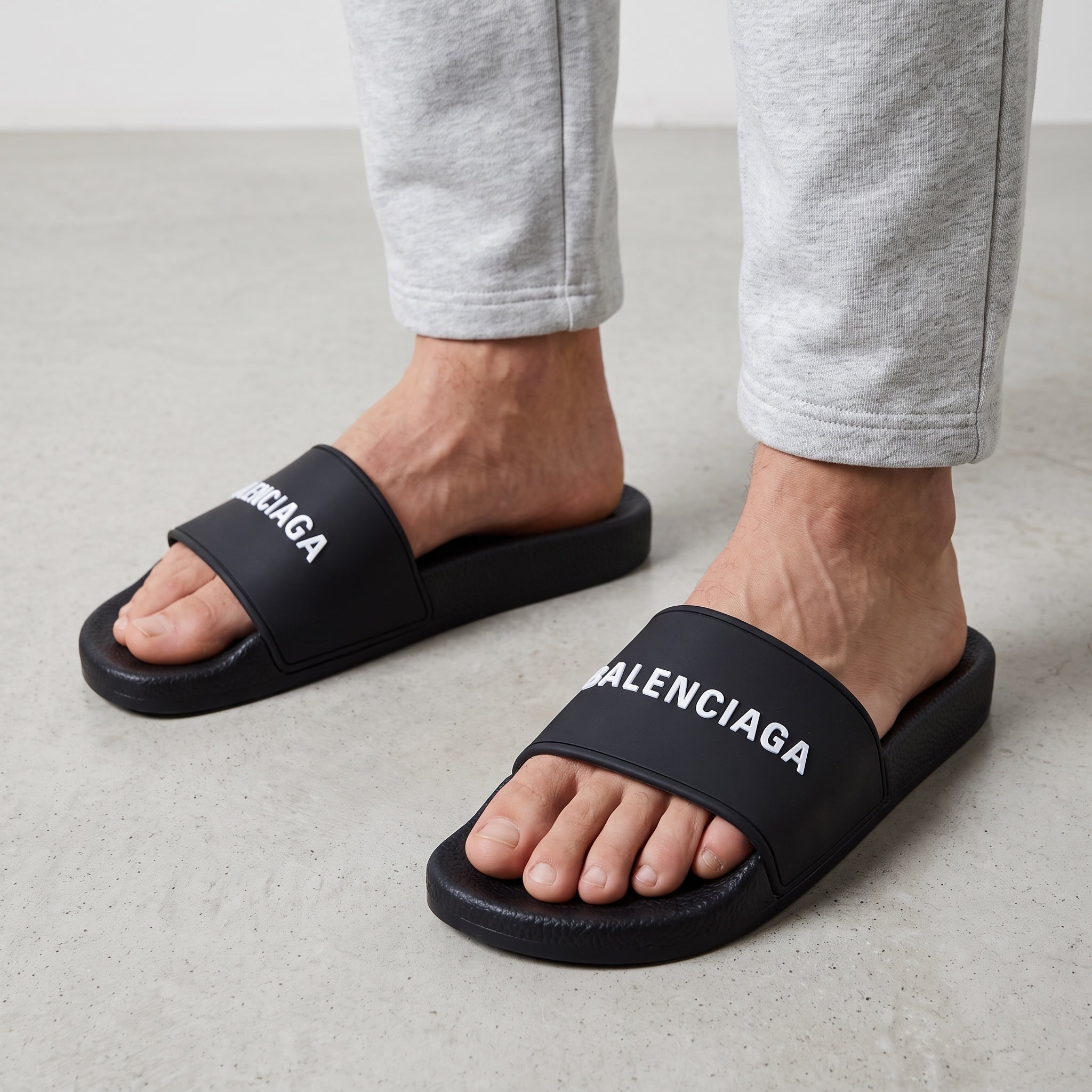 Black Balenciaga slides with raised white logo on wide strap and molded footbed