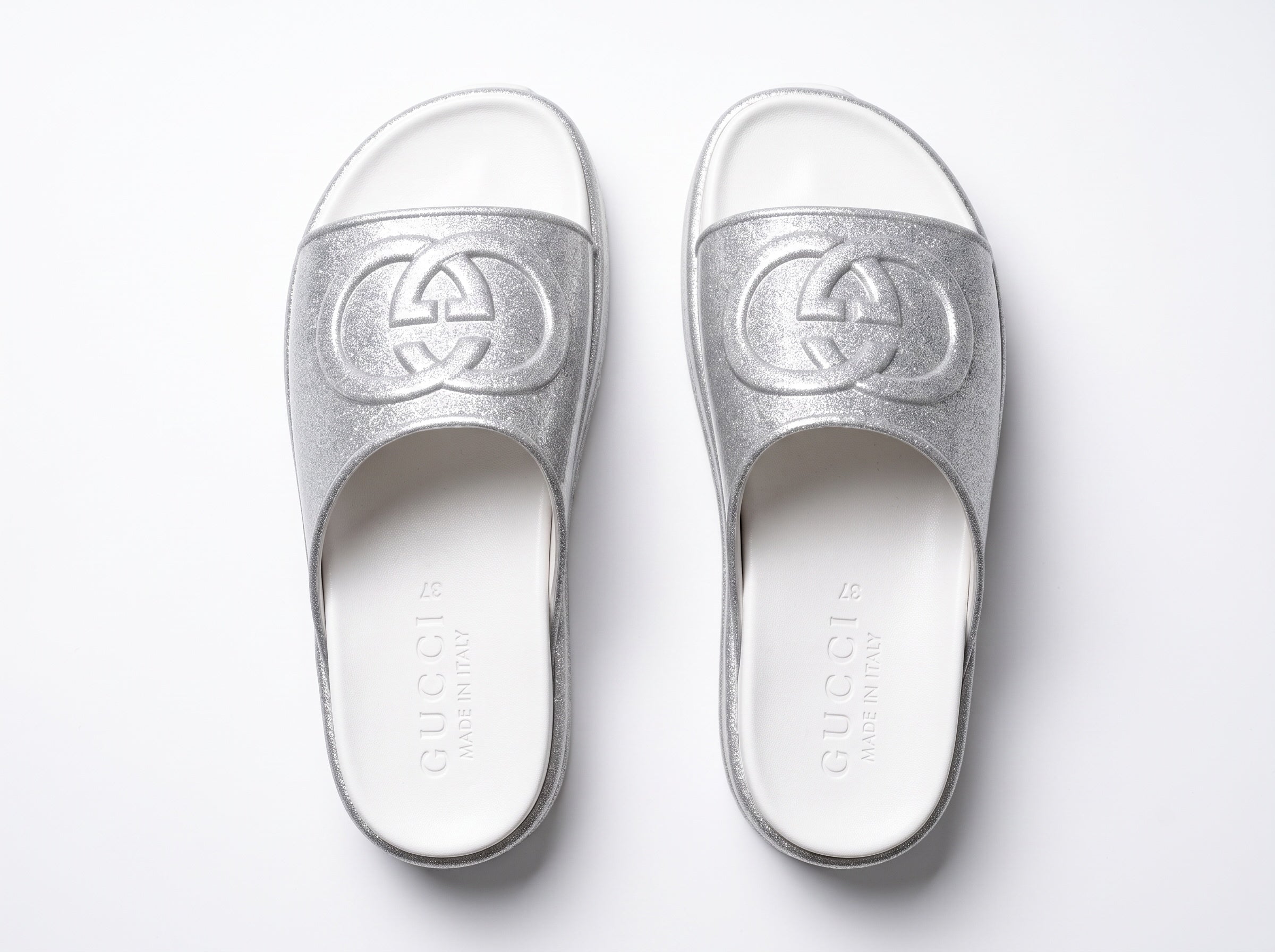 Silver Gucci flatform slides with glitter finish and raised interlocking G logo on white footbed