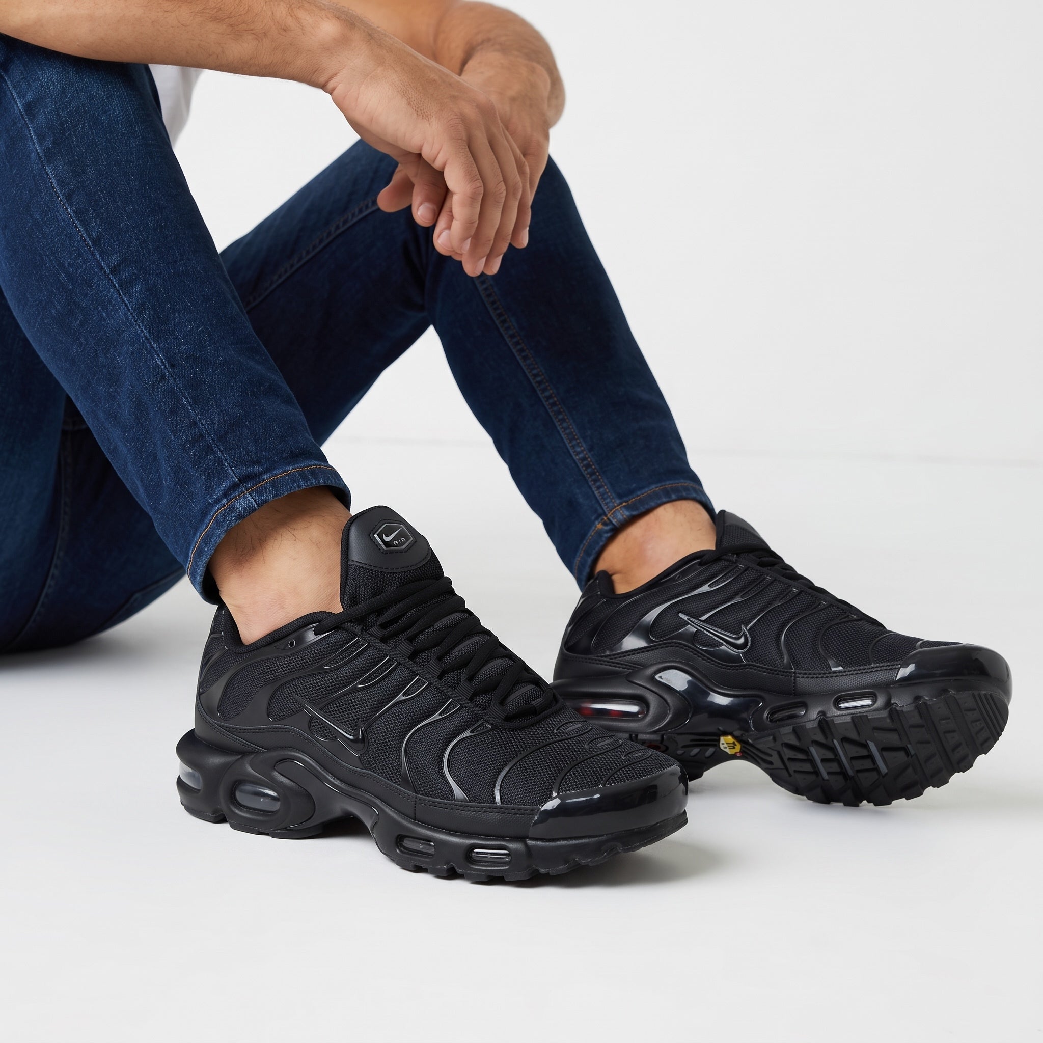 Nike Air Max Plus triple black sneakers with wavy overlays and visible Air units