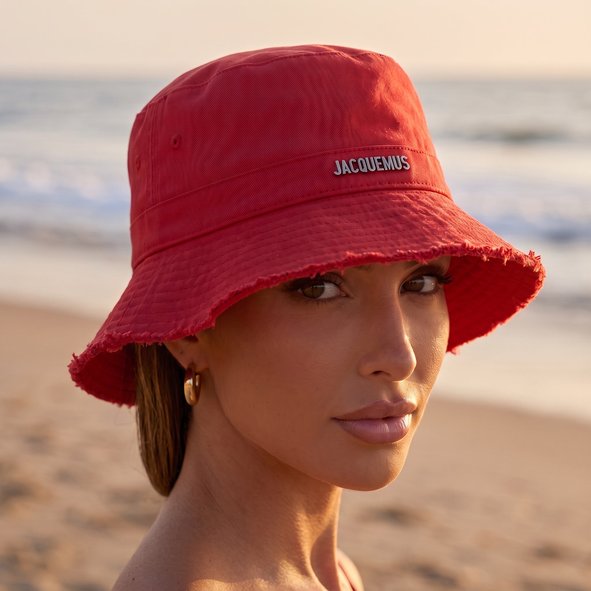 Red Jacquemus bucket hat with frayed brim and logo detail, worn at the beach