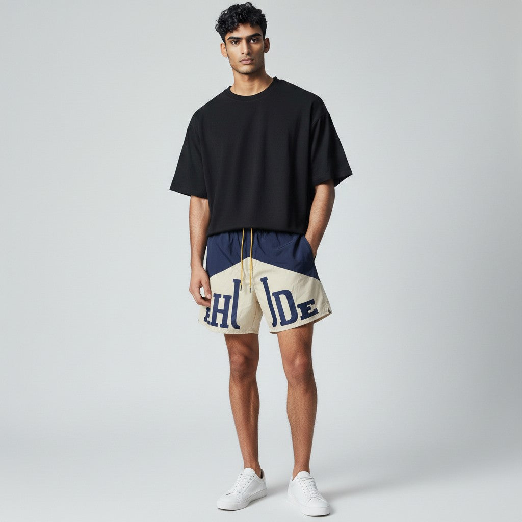 MASTERPIECE navy and cream Rhude swim shorts with oversized logo and yellow drawstring. Lightweight, fast-drying summer essential.