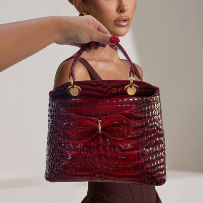 Red croc-embossed Dior tote bag with bow and gold rings held by model