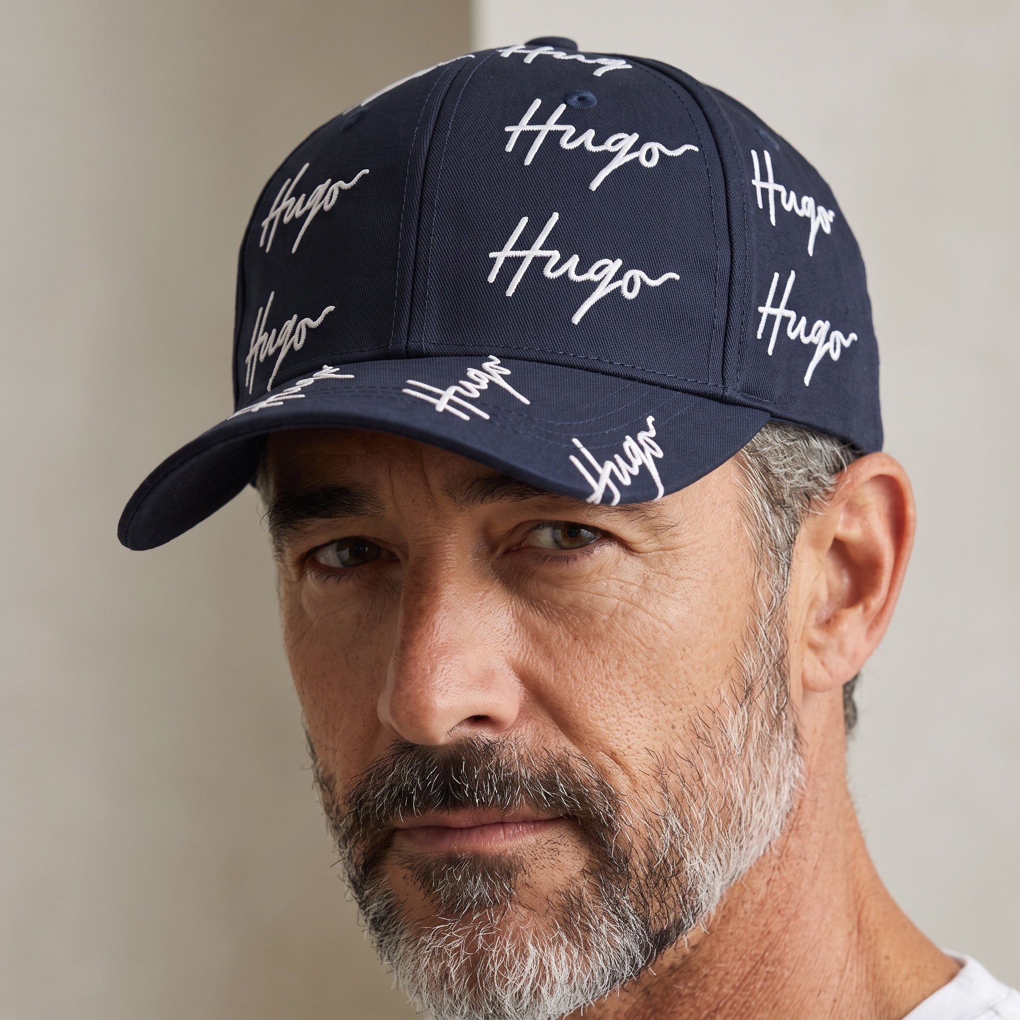 Man wearing a navy blue HUGO baseball cap with allover white embroidered logo script