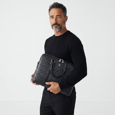 Man holding a black Louis Vuitton Damier briefcase with LV logo and silver zippers