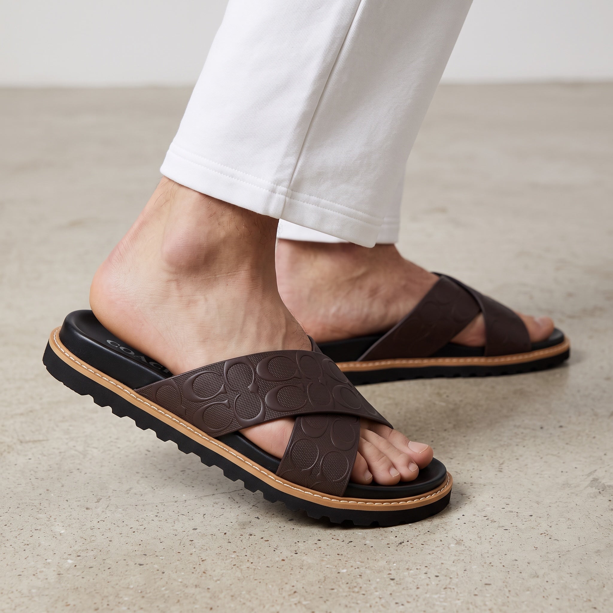 close-up of brown Coach crossover platform sandal with embossed logo straps