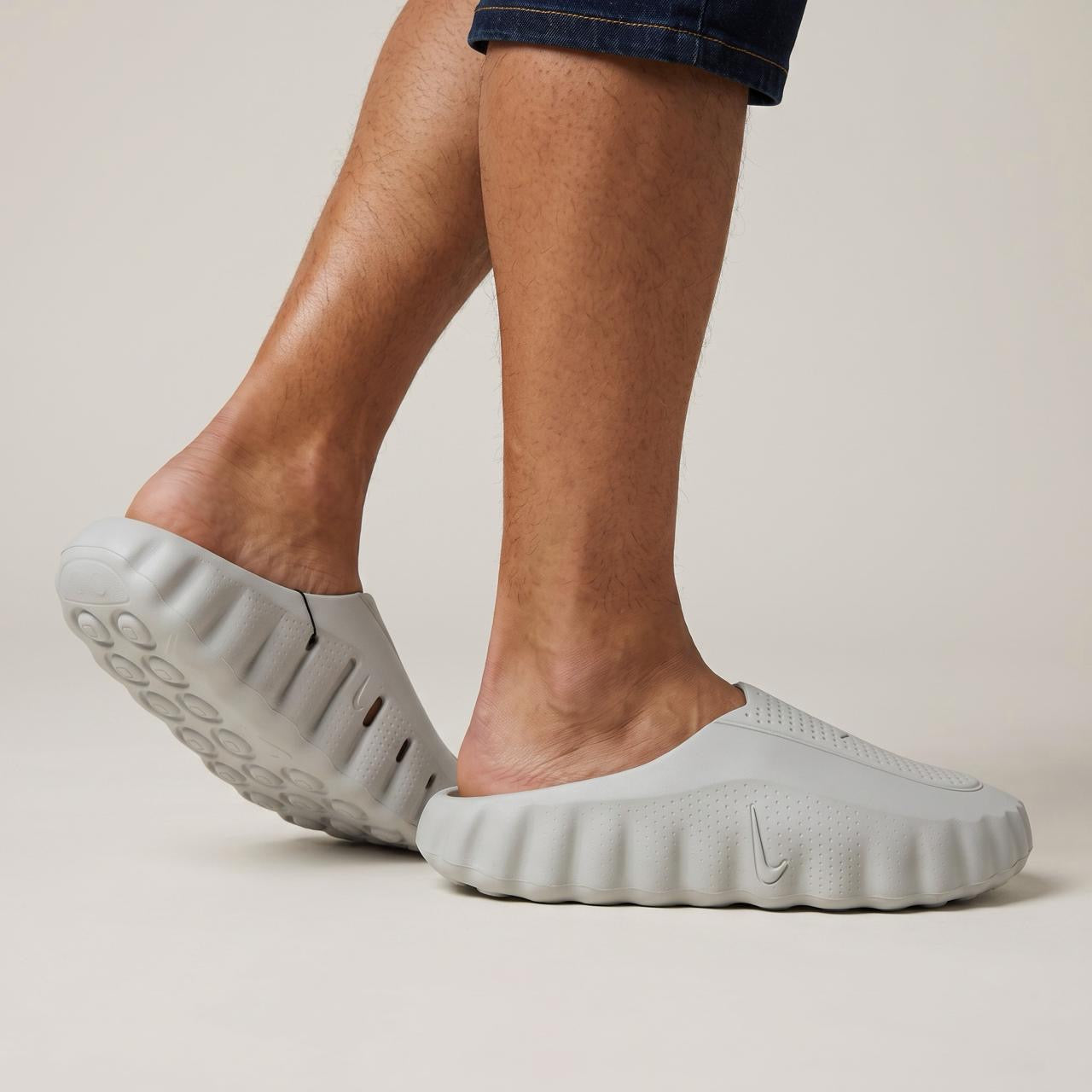 Pair of light grey Nike foam slip-on mules shown on feet