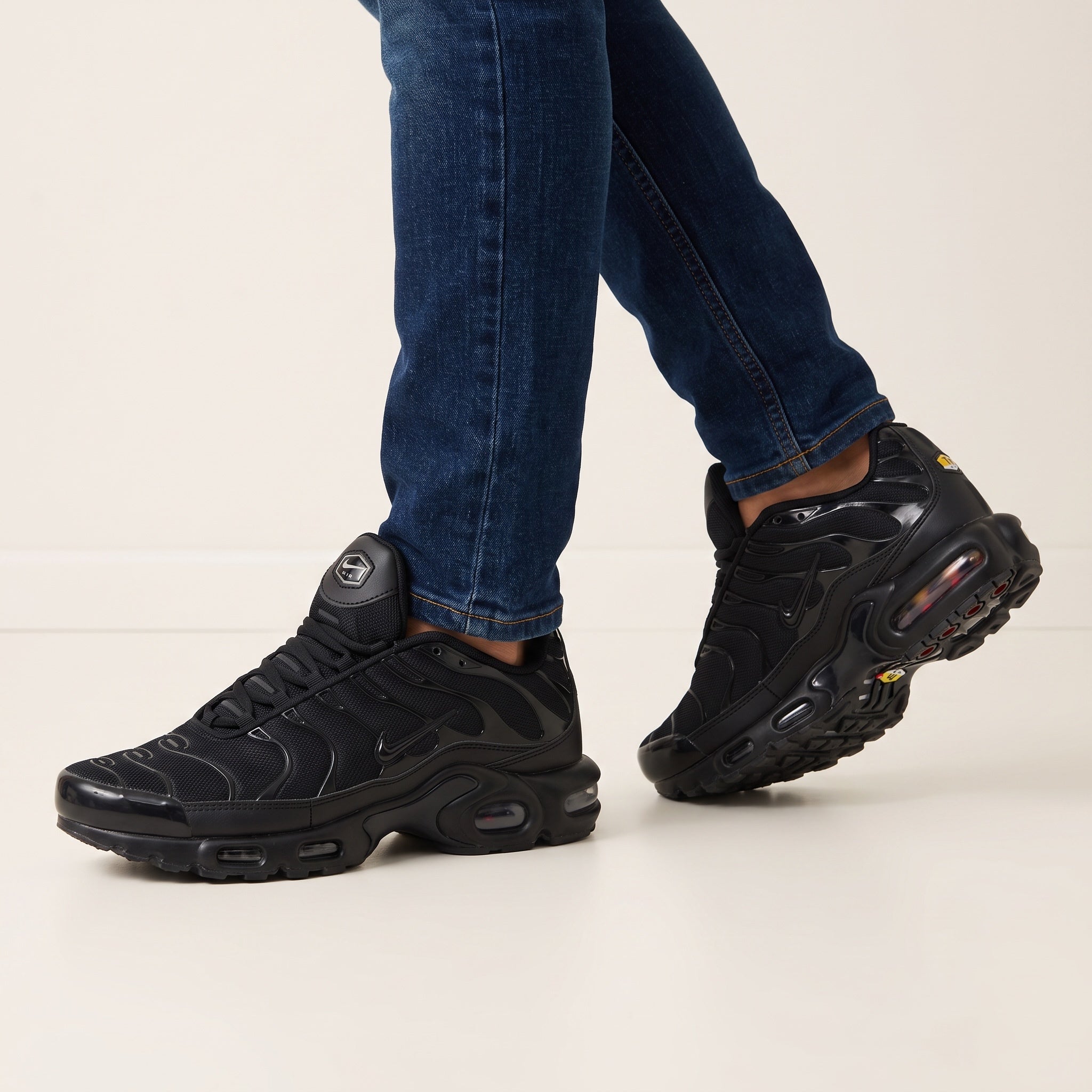 Nike Air Max Plus triple black sneakers with wavy overlays and visible Air units