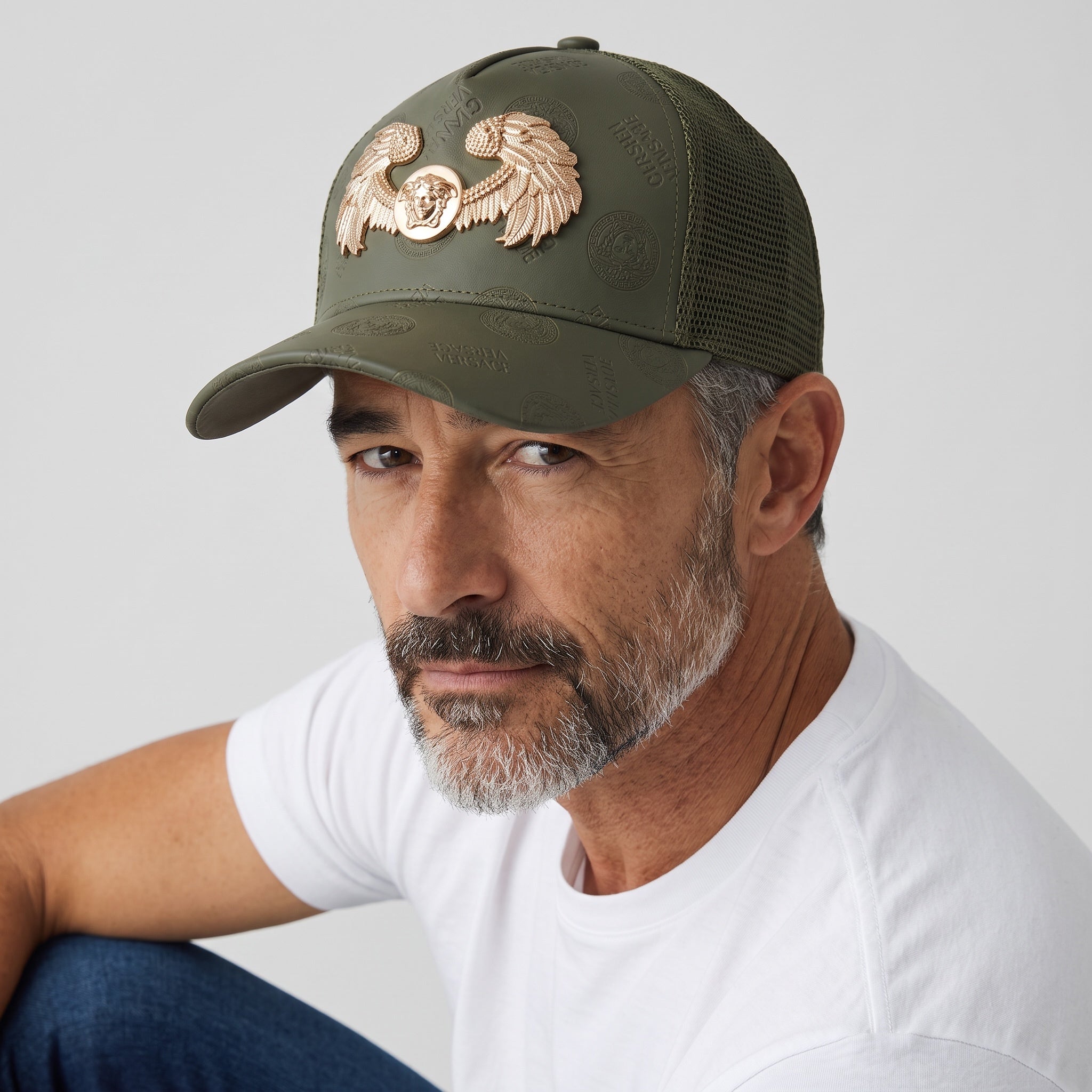 Olive green trucker cap with gold Medusa wings emblem and mesh back panel
