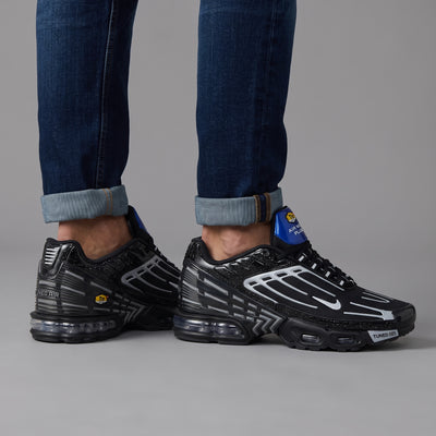 Pair of black Nike Air Max Plus Tuned Air sneakers with white overlays and blue heel tab