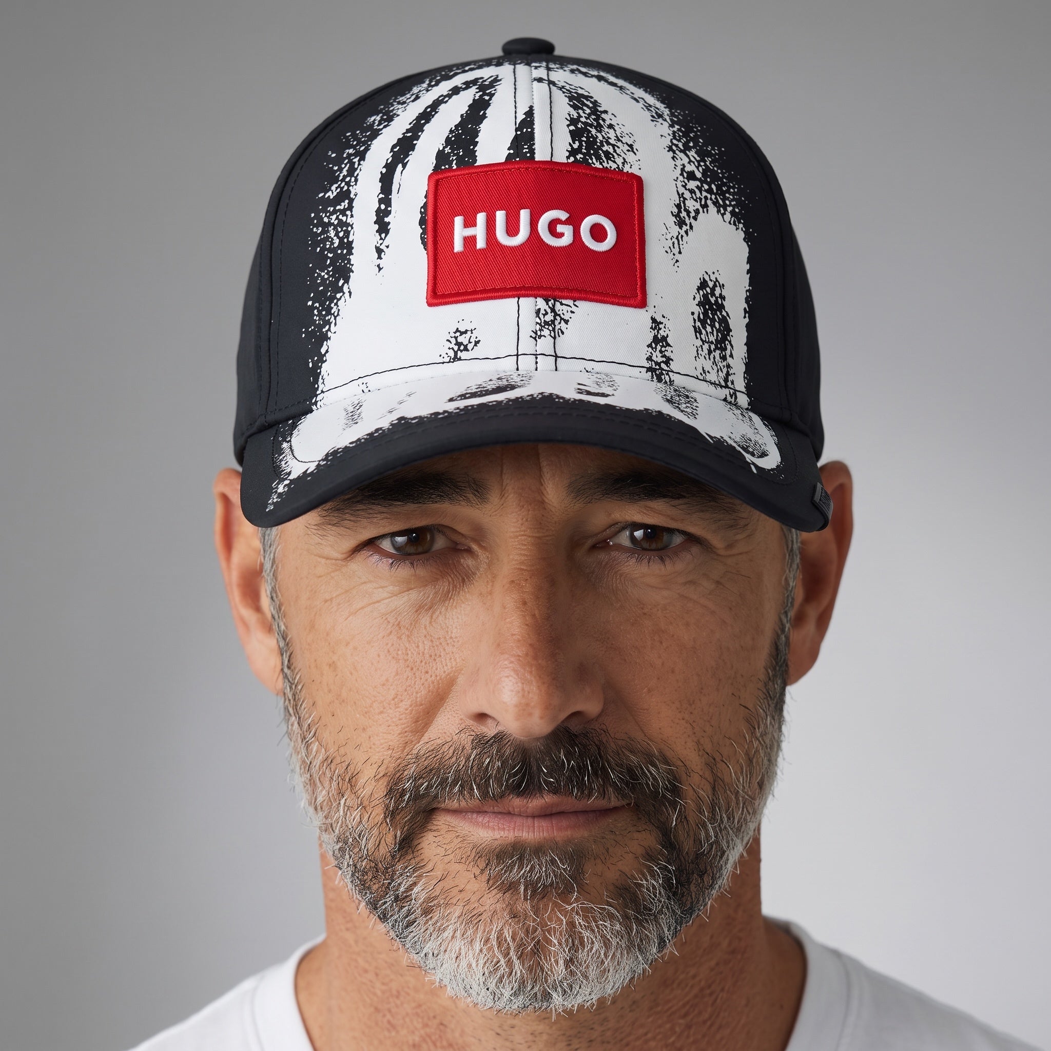 Man wearing a HUGO black and white brushstroke print baseball cap with red logo patch