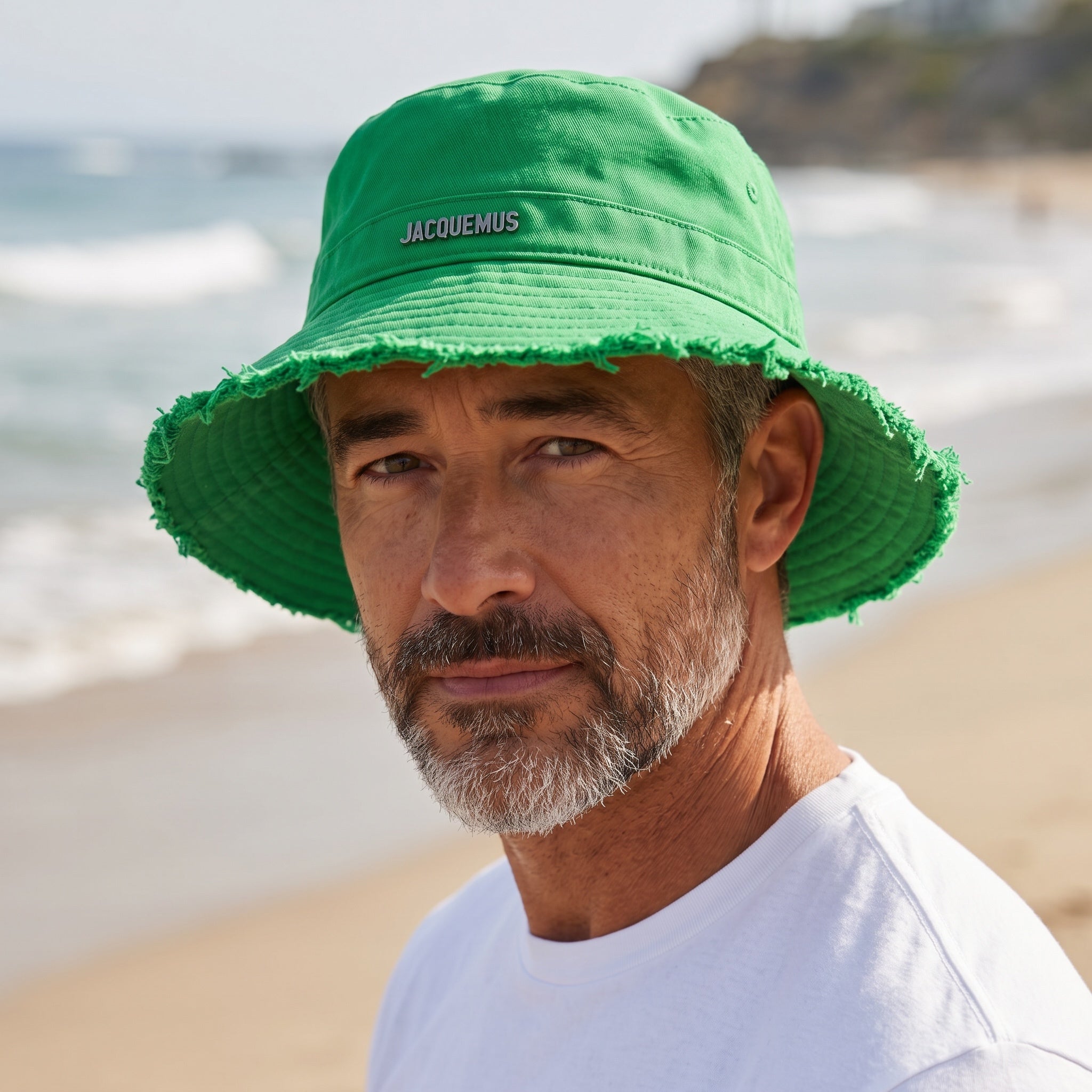 Green Jacquemus bucket hat with frayed brim and logo plaque, worn at the beach