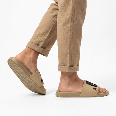 AMIRI beige rubber slides with black logo on model feet