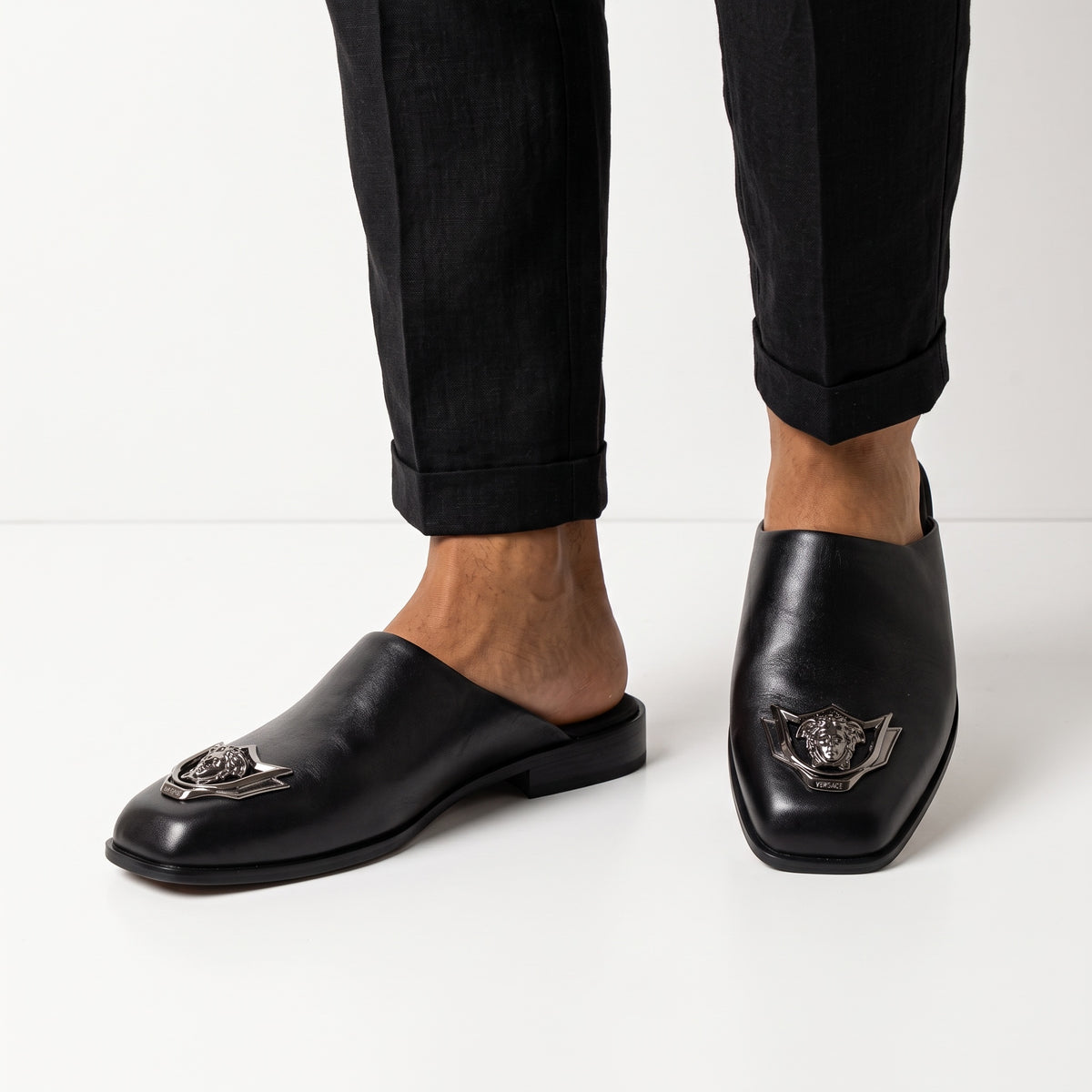 Black Versace mules with metal Medusa badge shown on model feet