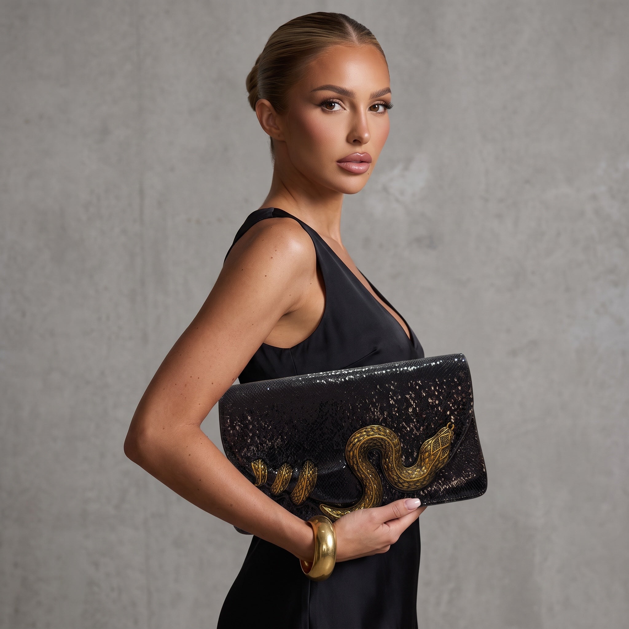 Black glossy clutch with large gold snake applique held by model