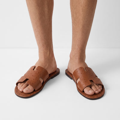 Hermès tan perforated leather men's slide sandals on model feet