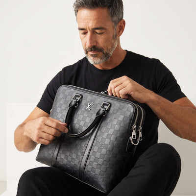 Man holding a black Louis Vuitton Damier briefcase with LV logo and silver zippers
